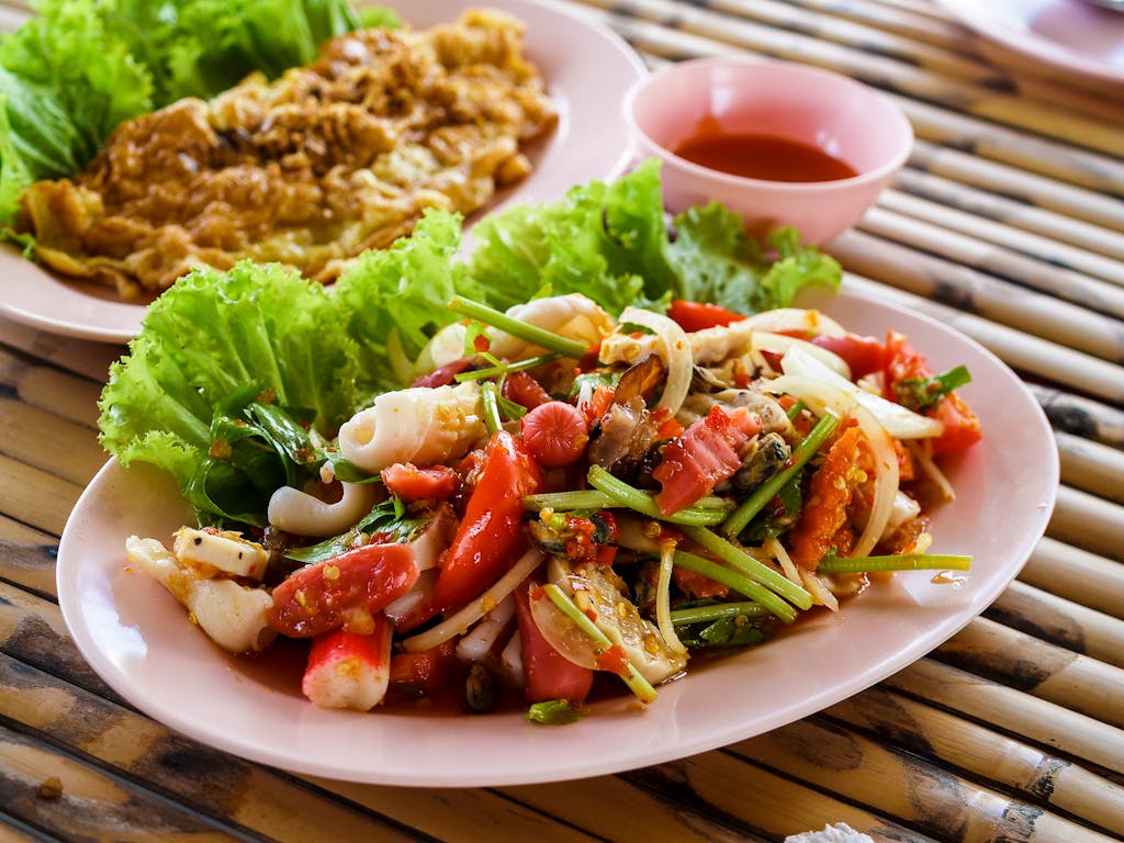Authentic Thai seafood salad with fresh vegetables and herbs served on a pink plate.