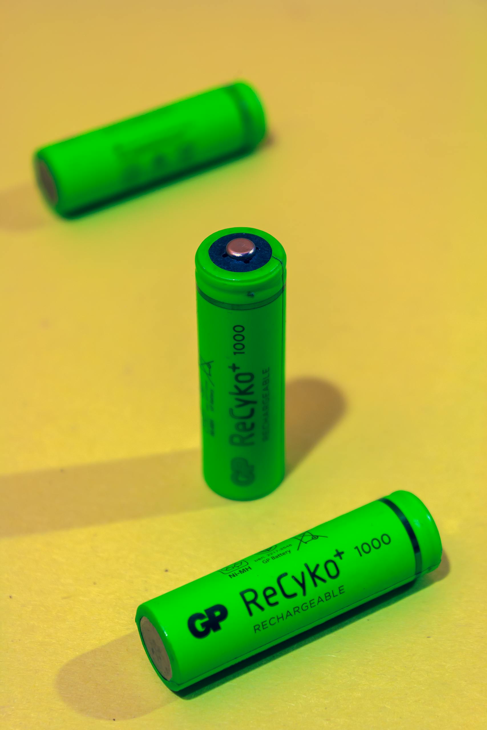 Close-up of green rechargeable batteries on a yellow background, emphasizing energy and recycling.