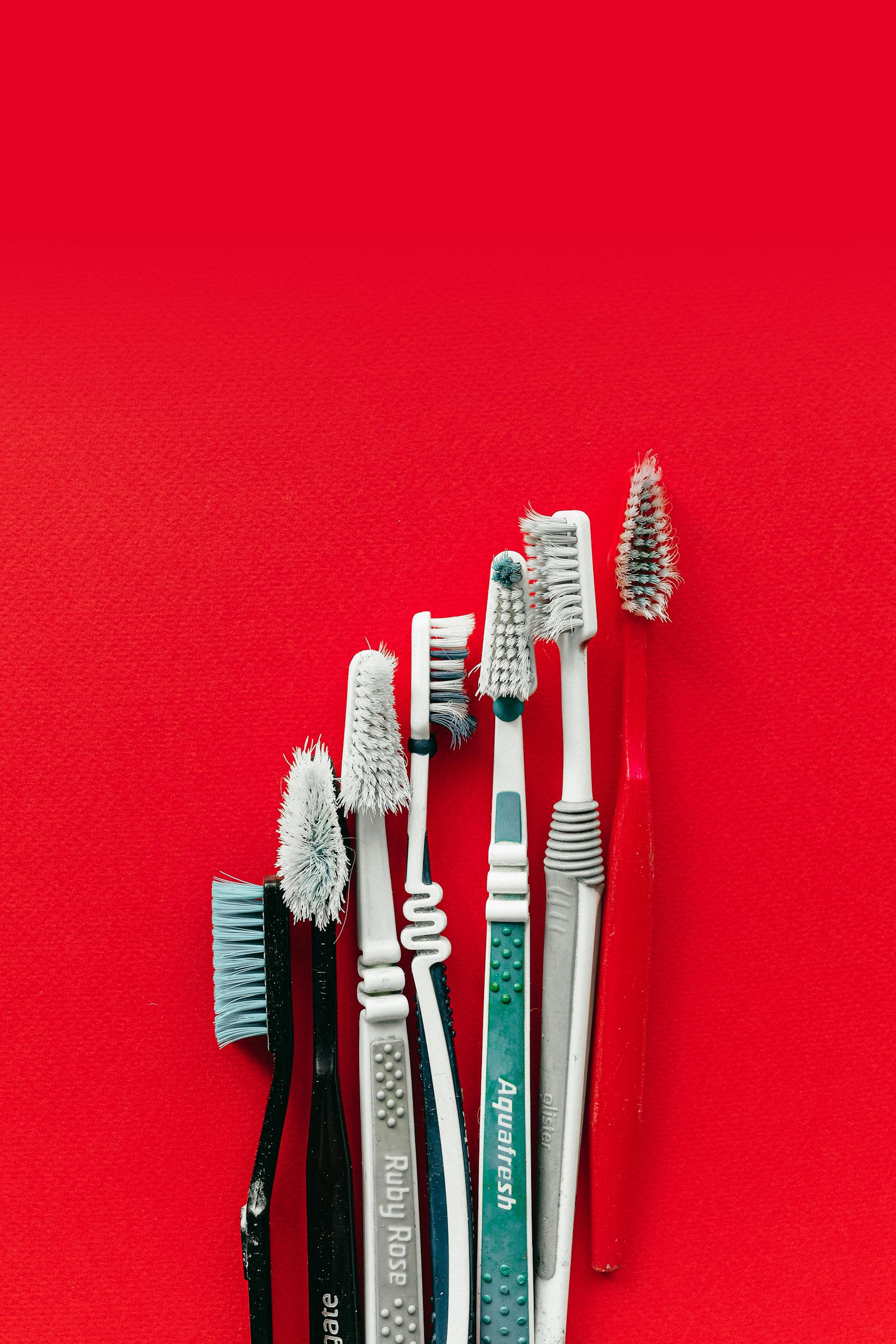 Collection of old and worn toothbrushes on a bright red background, highlighting dental hygiene concepts.