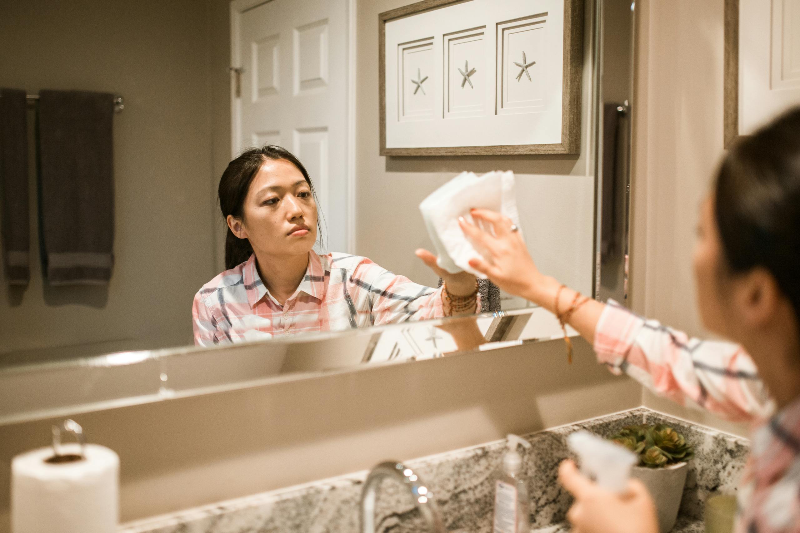 Focused woman cleaning a bathroom mirror, reflecting dedication to house chores.