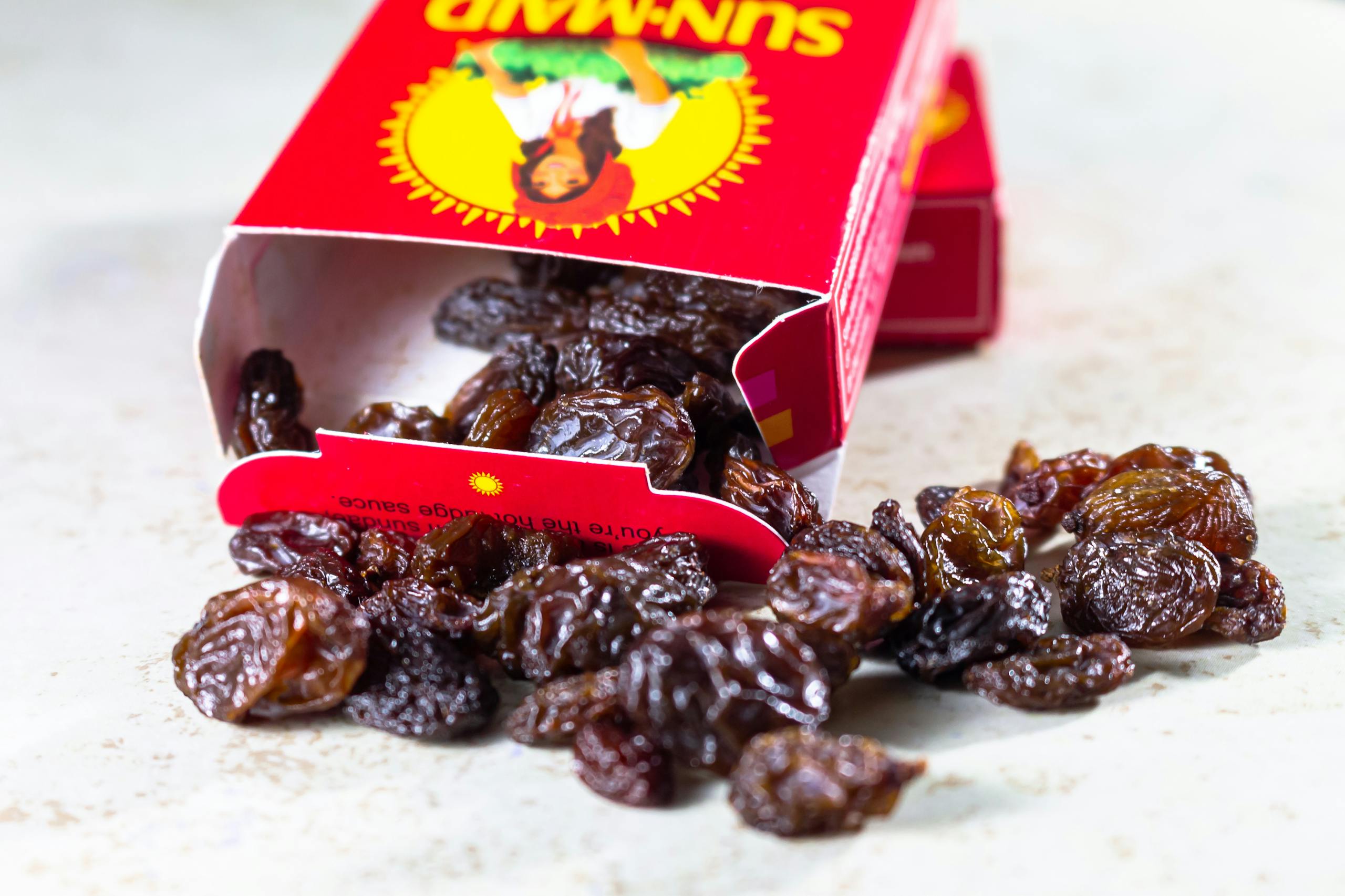 A close-up view of an open box spilling raisins onto a light surface.