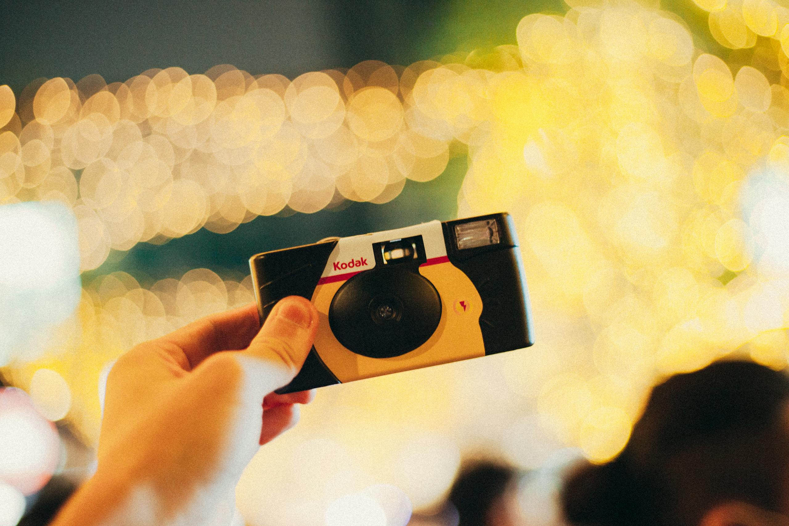 A disposable camera is held up against a vibrant bokeh background, capturing a nostalgic moment.