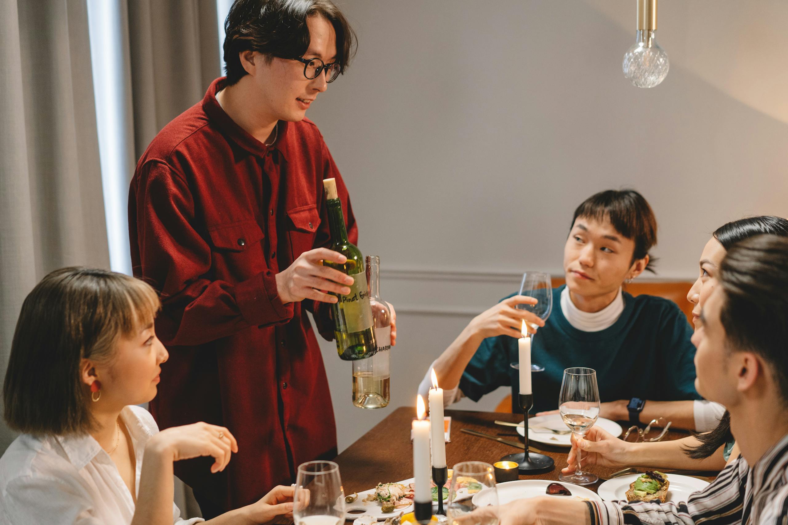 A group of friends enjoying a cozy dinner with wine and candlelight indoors.