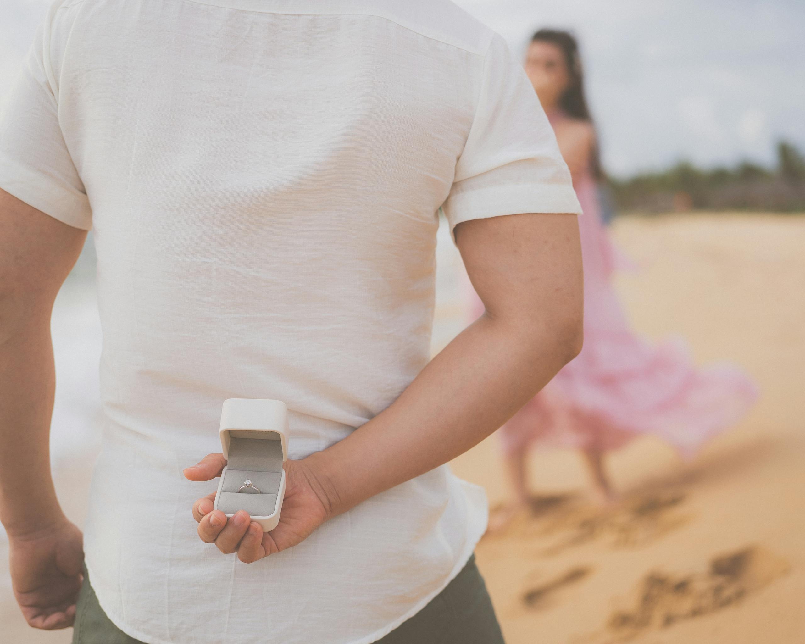 A man hides an engagement ring behind his back, preparing to propose on a beach in Phu Quoc.