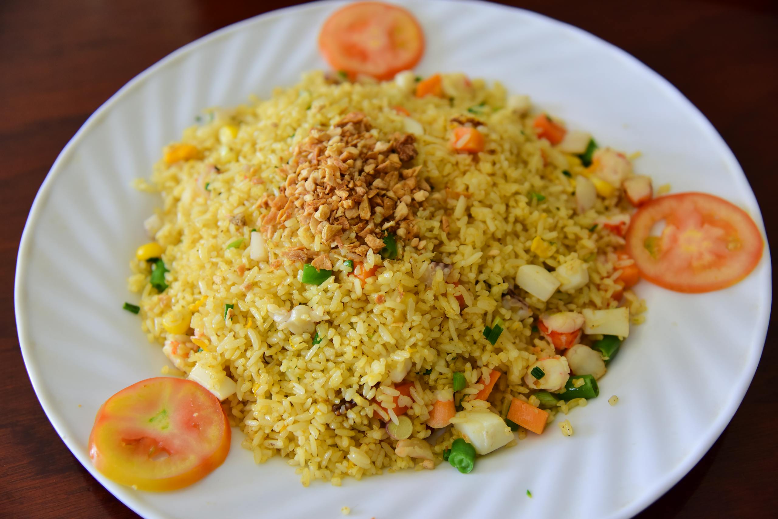 A mouth-watering plate of vegetable fried rice, garnished with fresh tomatoes.