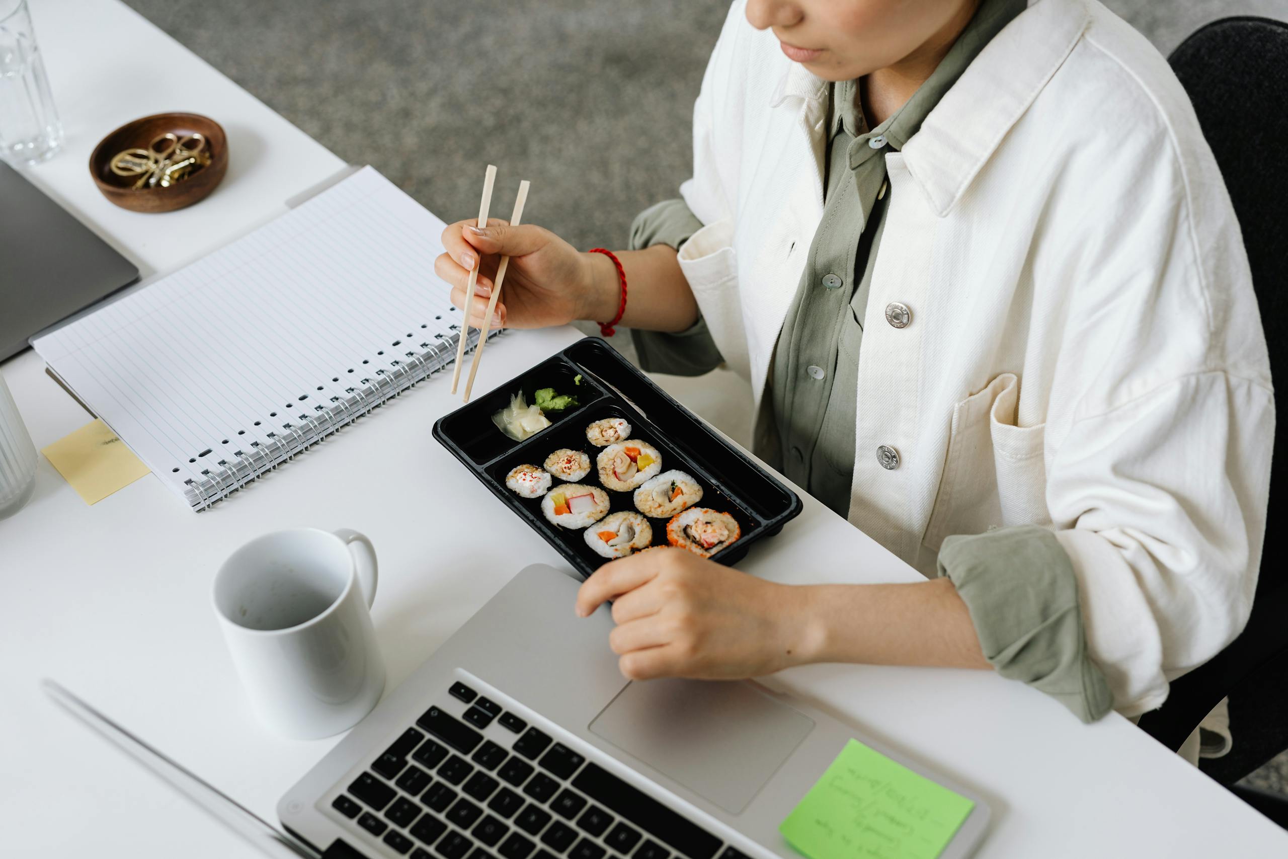 A person enjoying sushi with chopsticks at a work desk, captured from above.