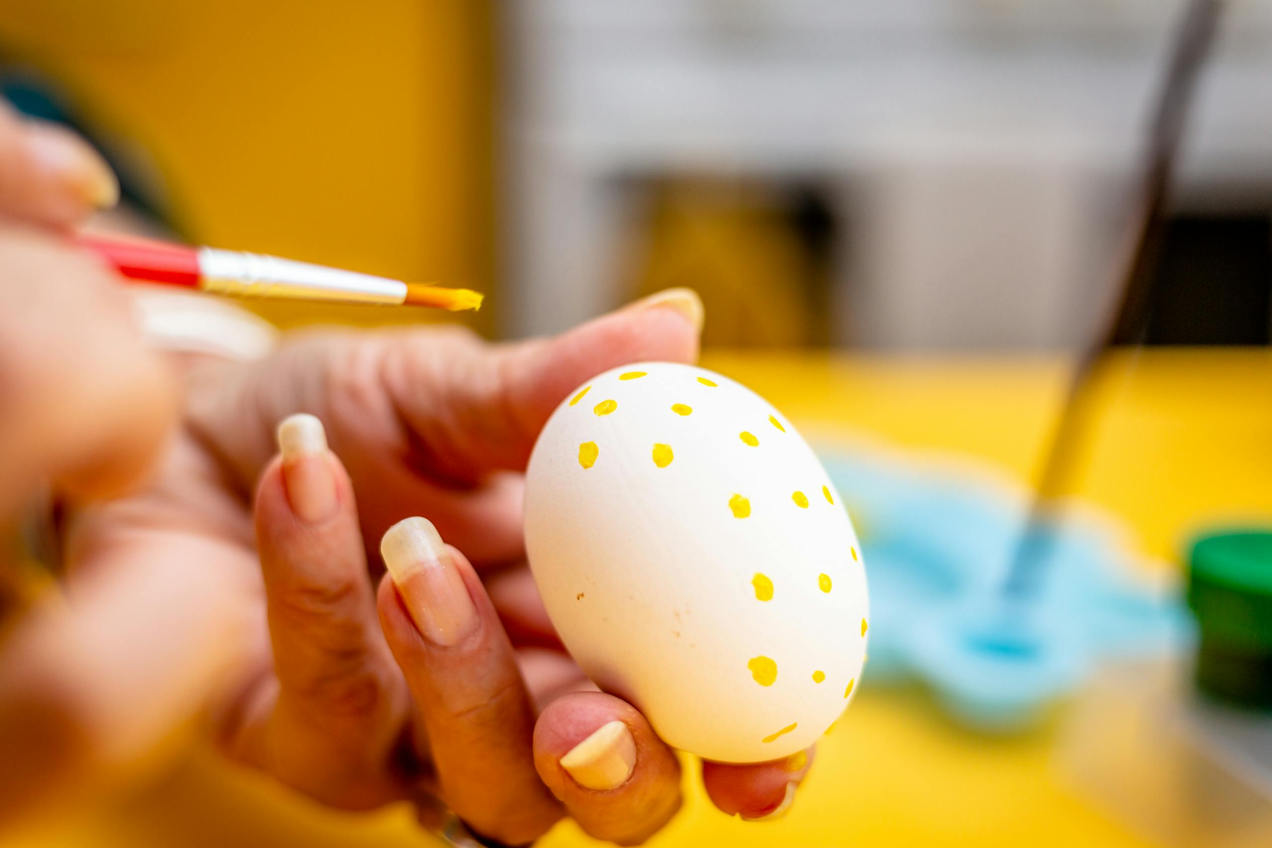 A person painting small yellow dots on an Easter egg using a brush. Perfect for Easter themes.