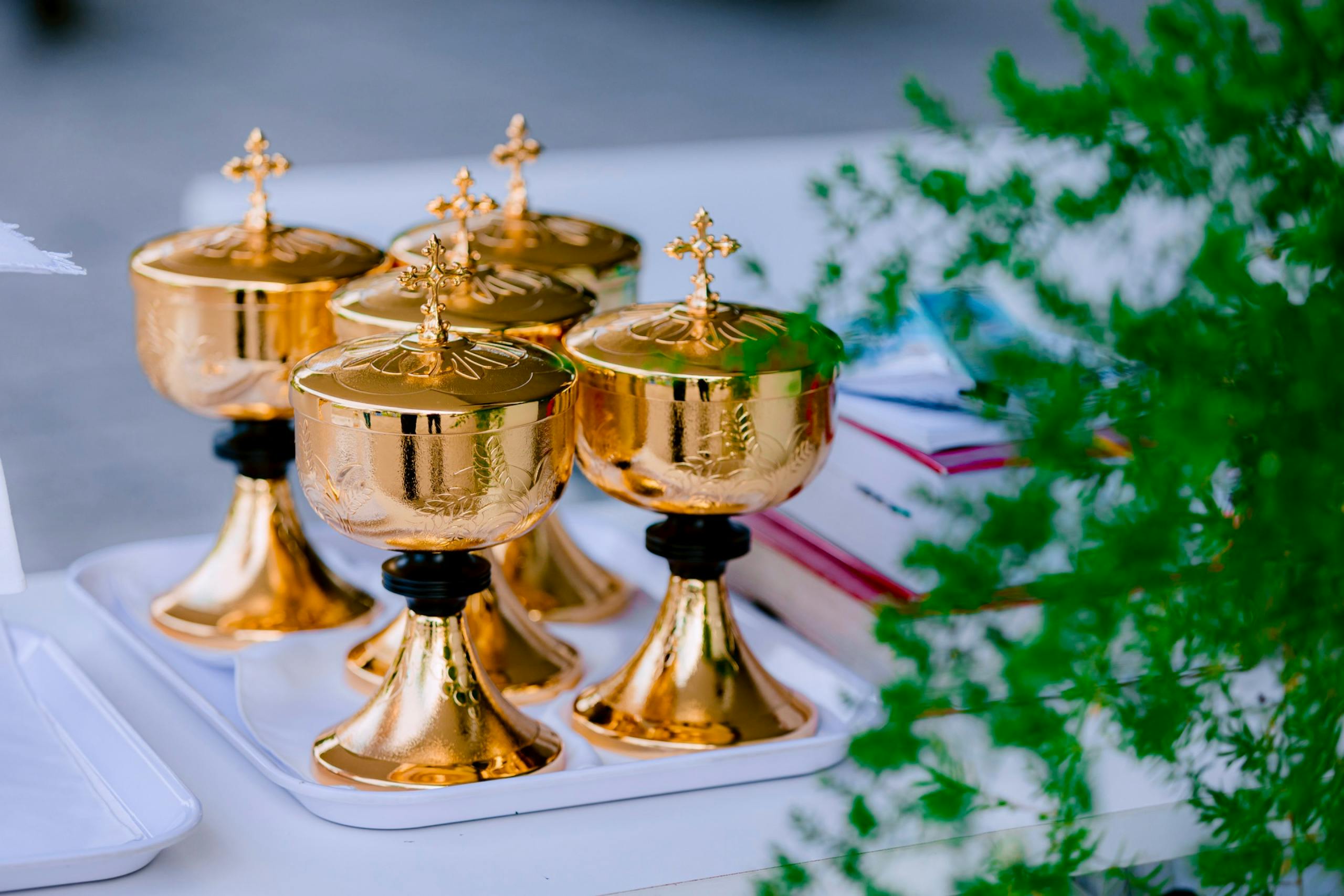 A set of golden communion chalices on an altar table outdoors, surrounded by greenery.