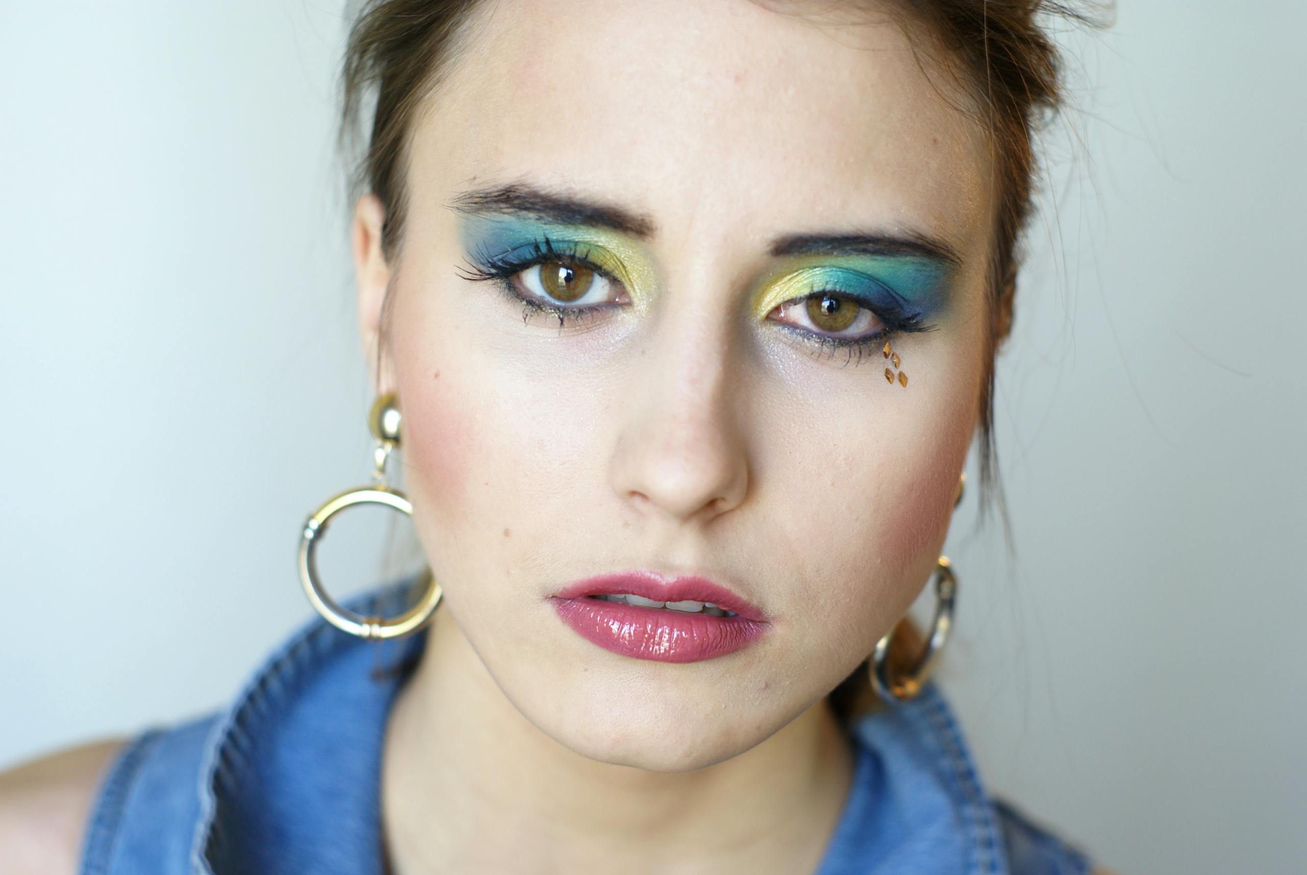 A striking close-up of a woman showcasing vibrant eye makeup and glossy lips.
