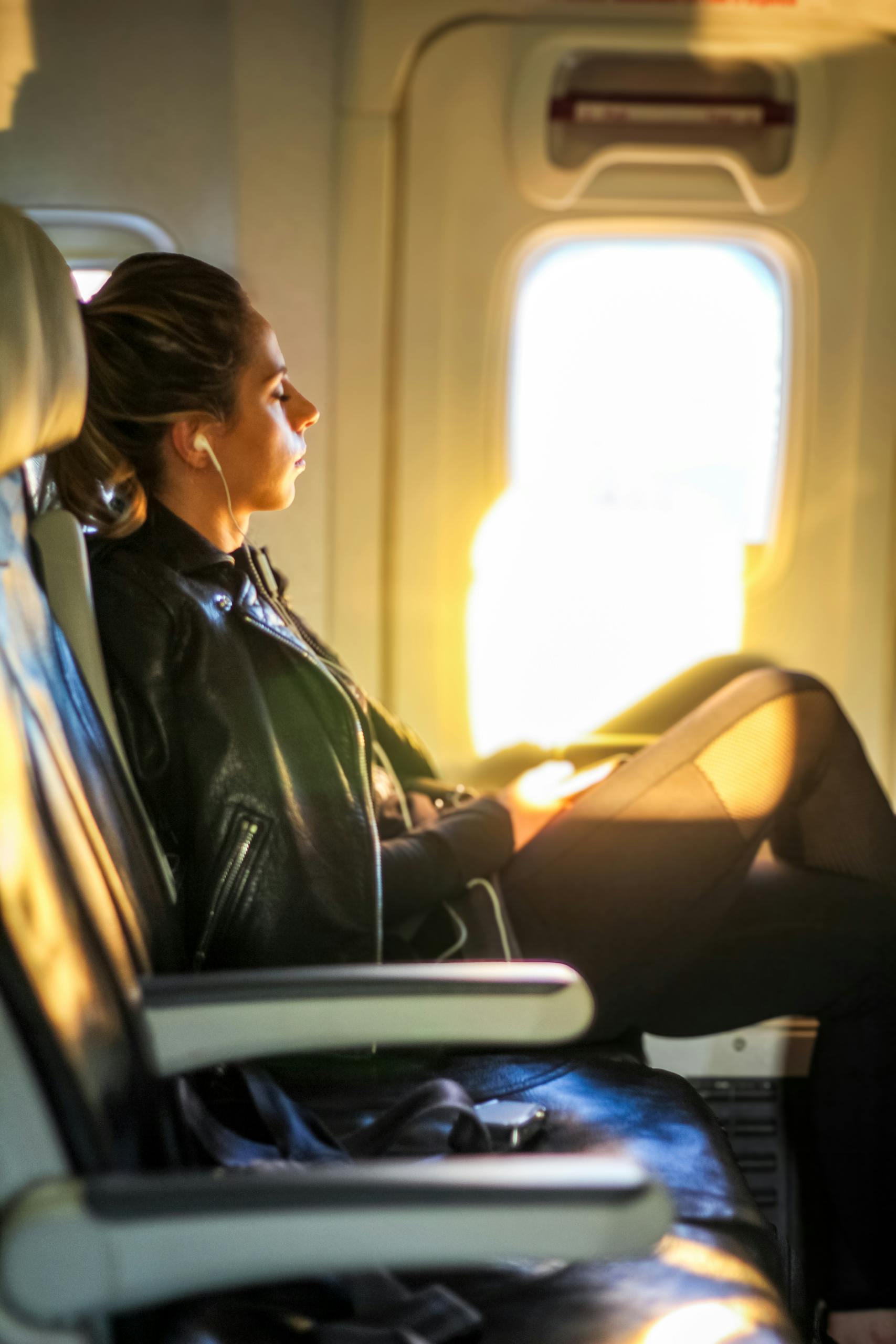 A woman enjoys a tranquil moment on a flight, gazing out the window with headphones on.