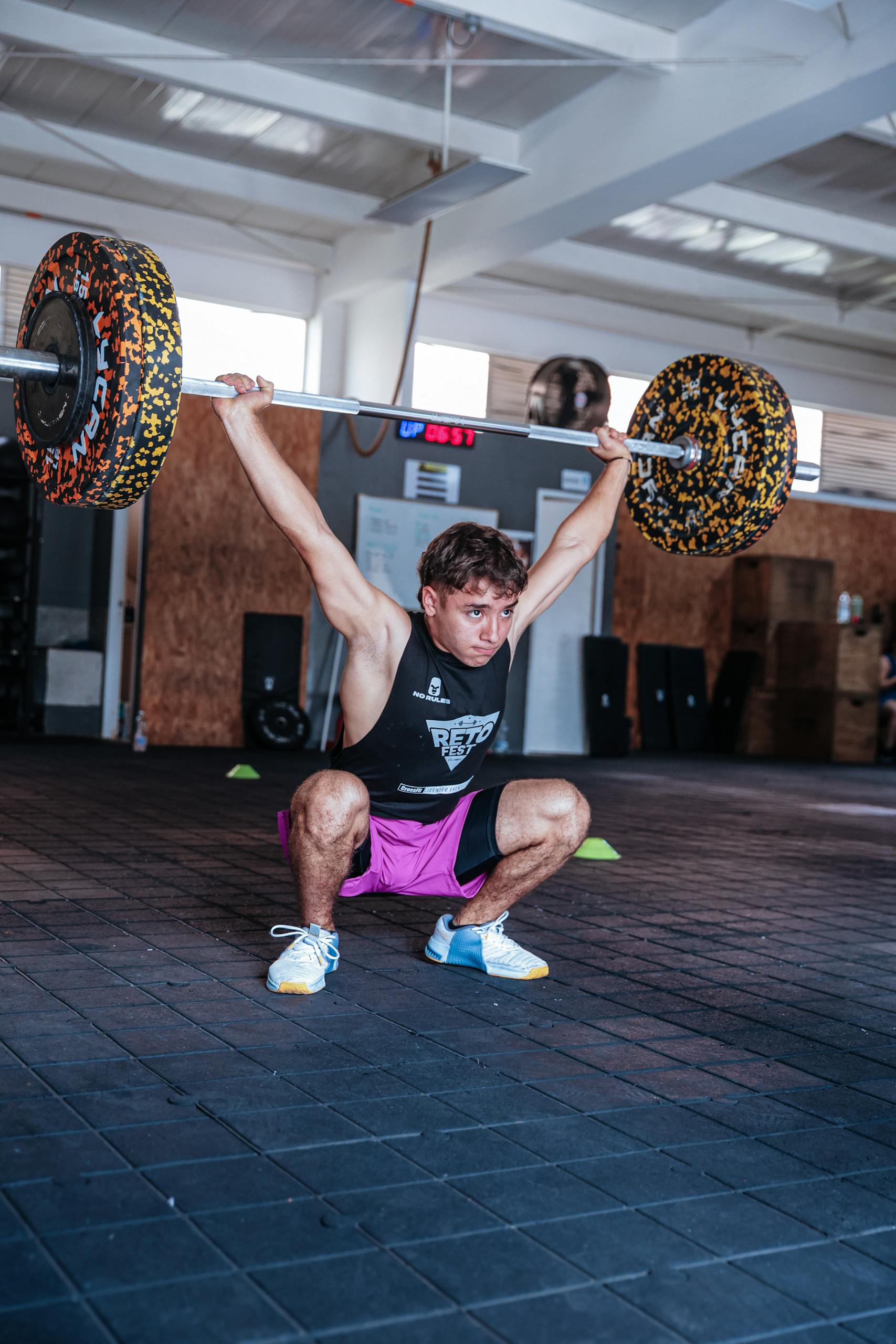 A young man lifting heavy weights overhead in a gym setting, showcasing strength and athleticism.