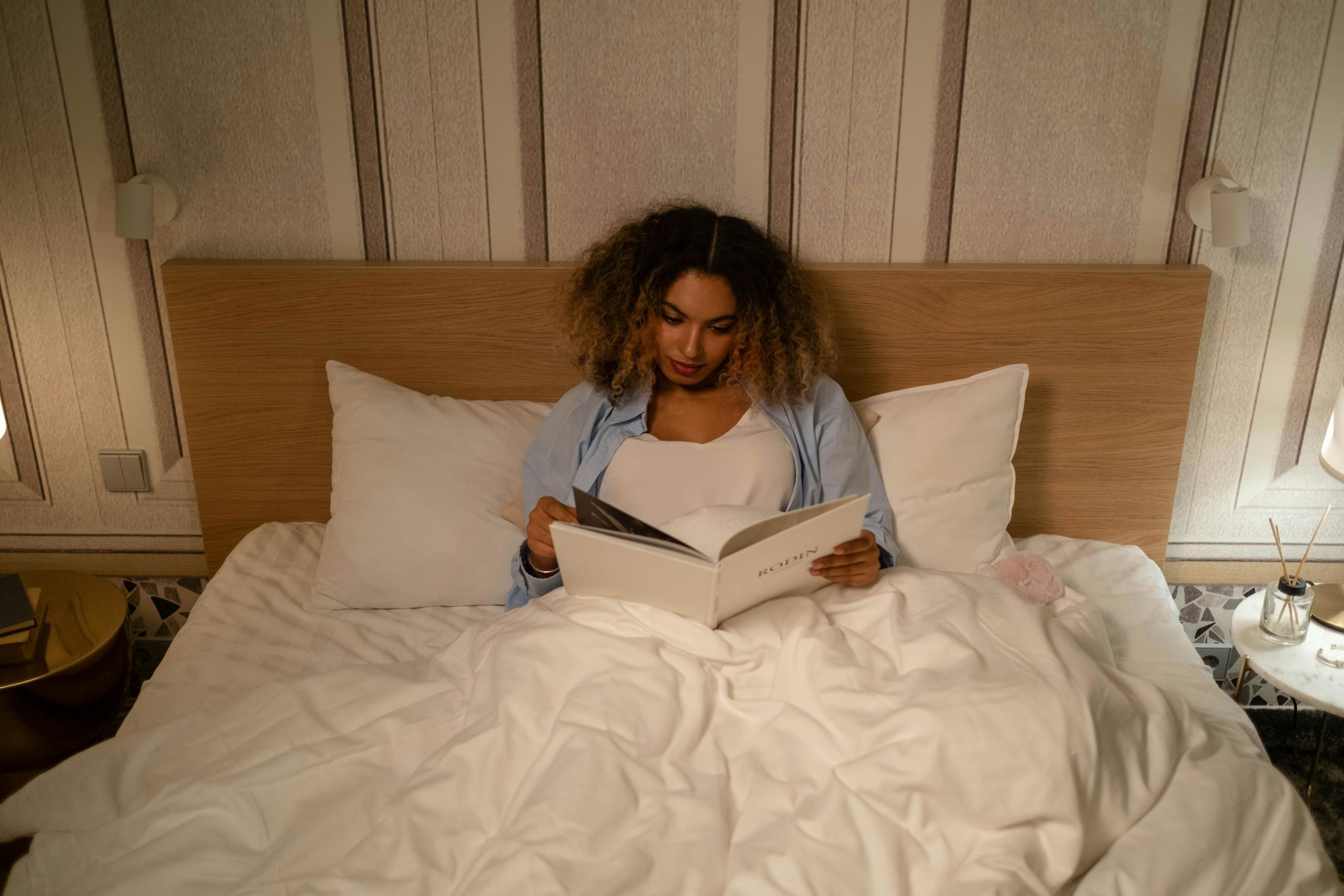 African American woman enjoys a peaceful evening reading in bed, capturing a moment of leisure and relaxation.