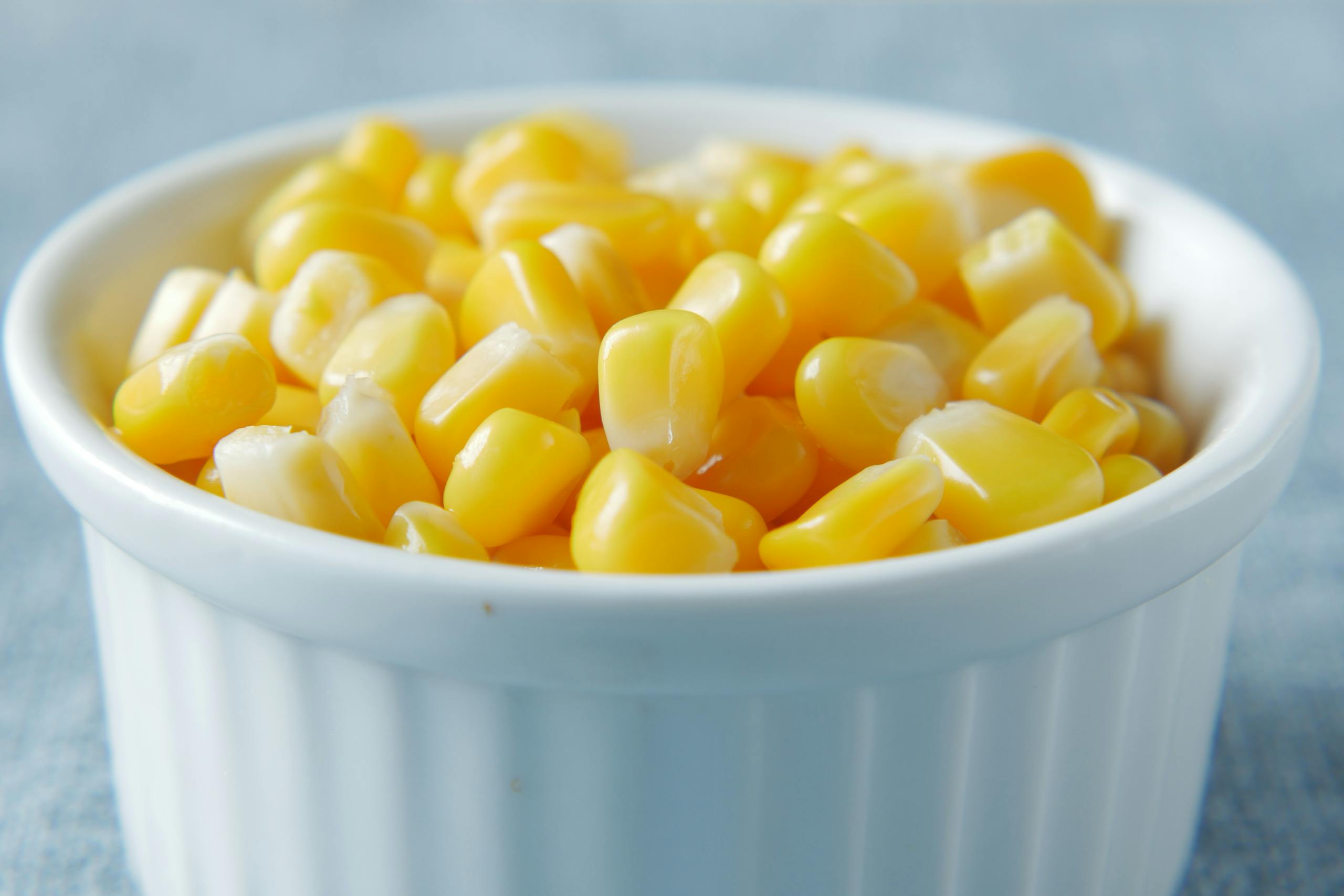 Close-up of vibrant yellow corn kernels in a white ceramic bowl, showcasing a healthy snack.