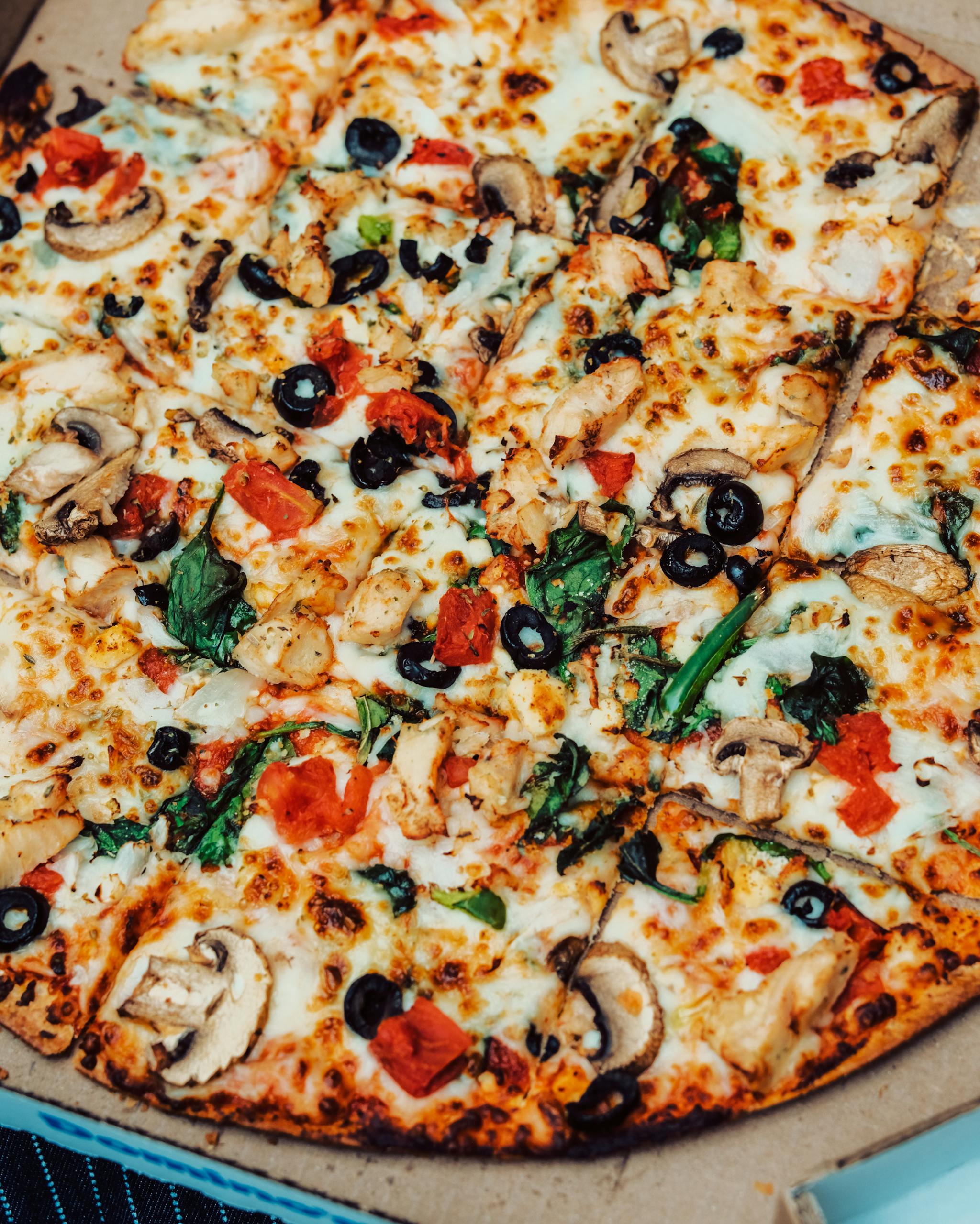 Closeup of a fresh vegetable and cheese pizza in a cardboard box, ready to eat.