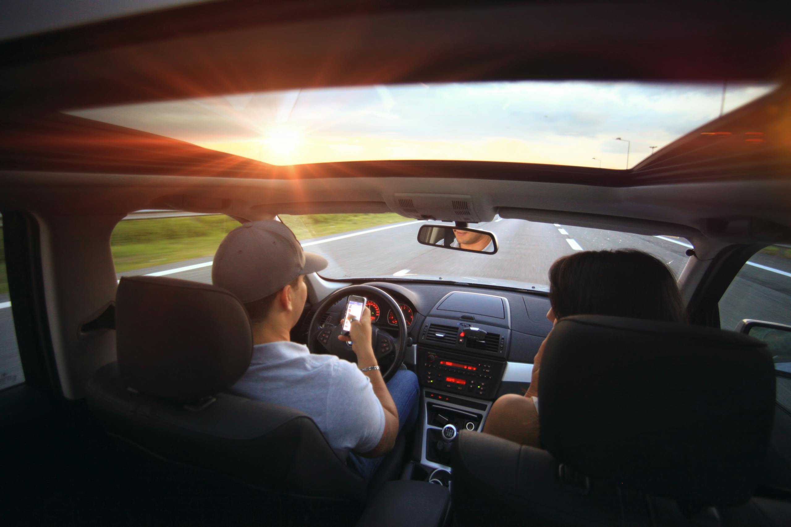 Driver using phone while driving at sunset with passenger in vehicle.