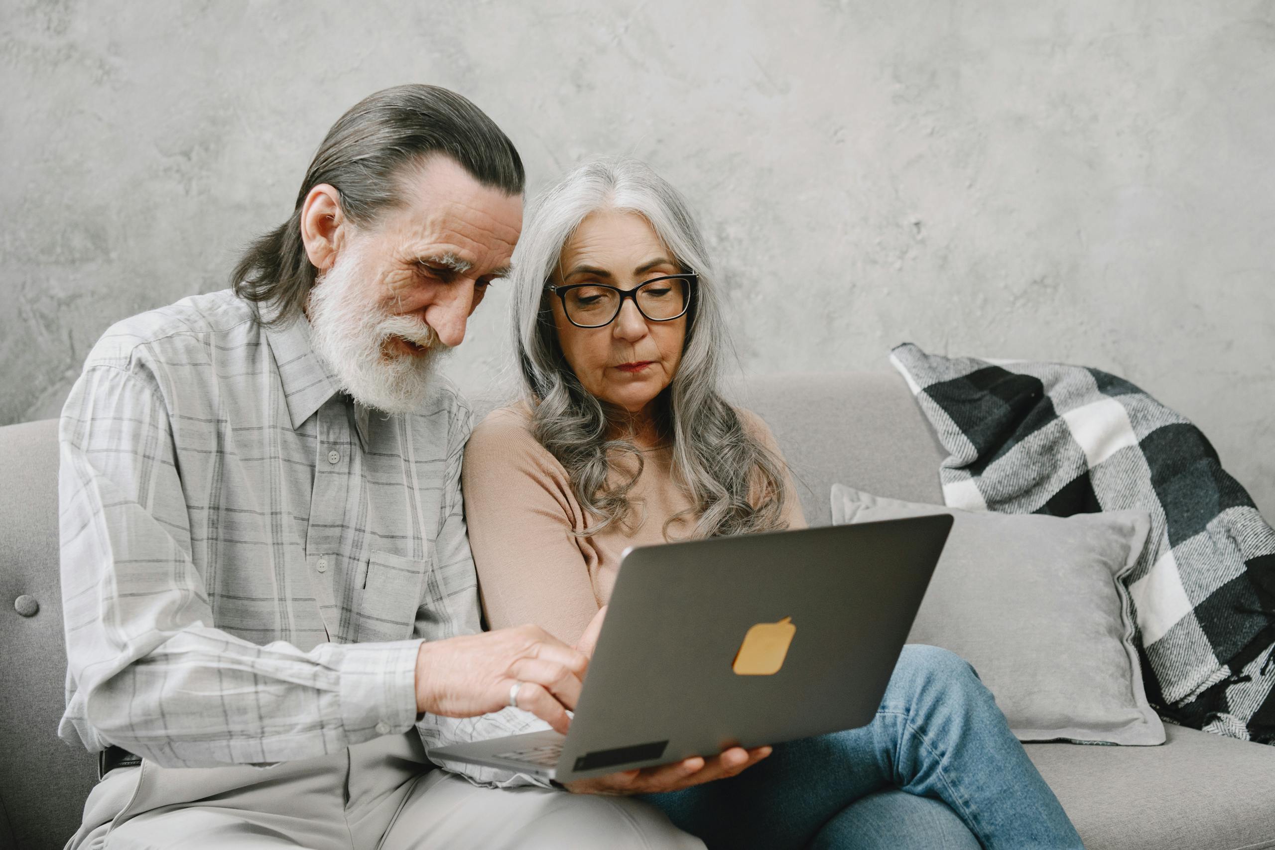 Elderly couple sitting on a couch using a laptop, sharing a moment of togetherness.
