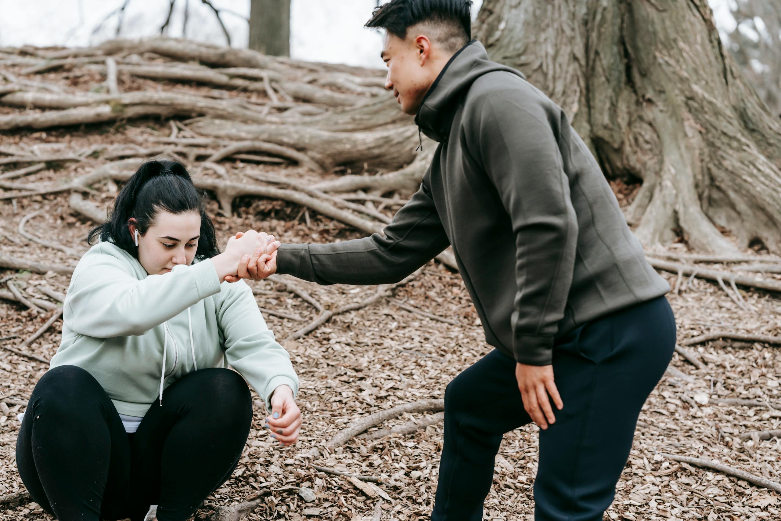 Ethnic man in sportswear helping overweight female with dark hair get up from ground in park in daytime