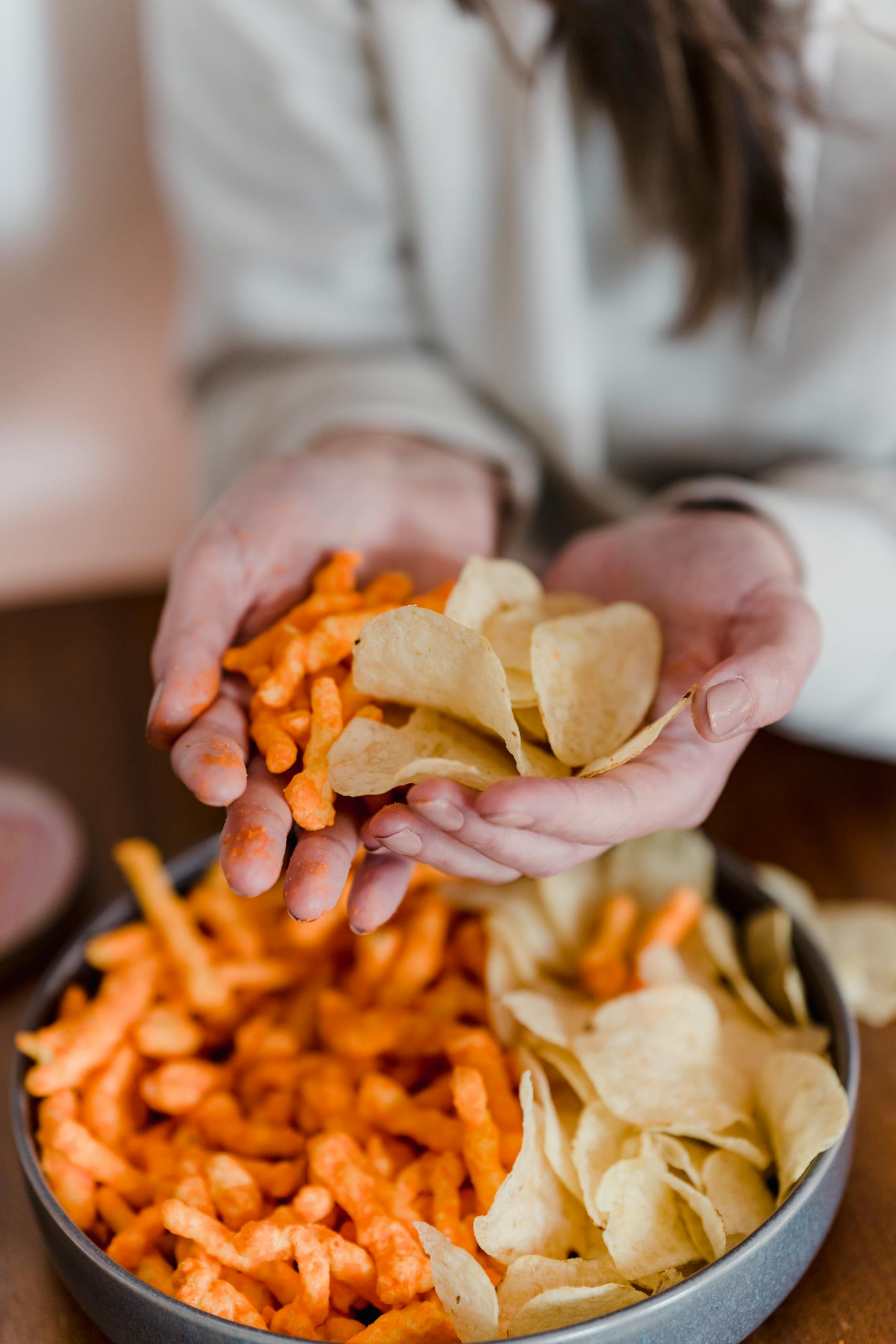 From above of crop unrecognizable female holding chips and corn snacks in hands in daytime