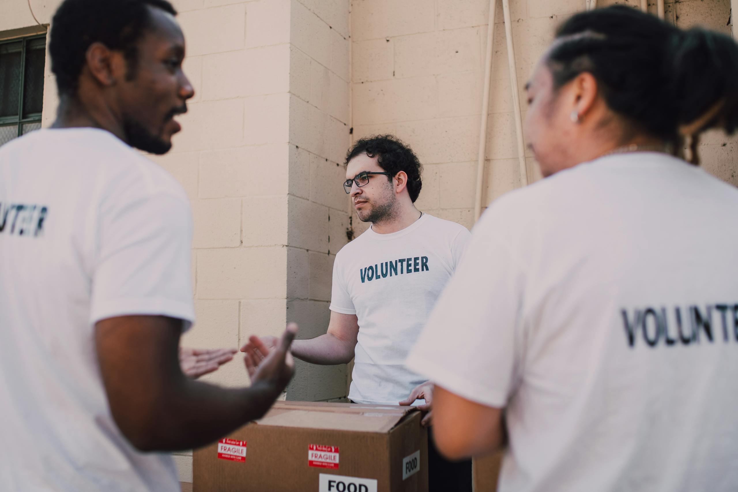 Group of diverse volunteers organizing food donations in white shirts marked with 'Volunteer'.