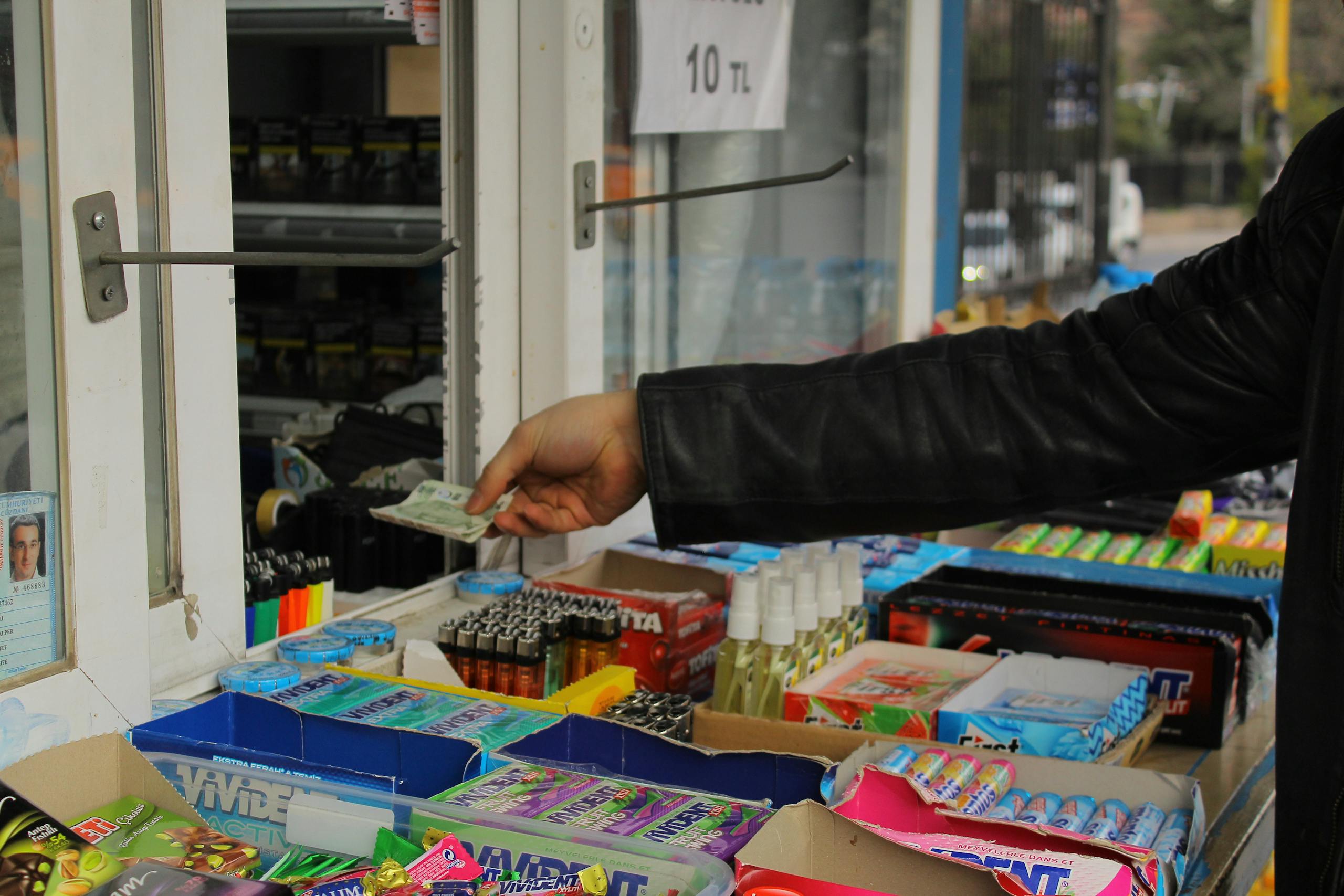 Hand giving cash at a kiosk counter filled with various small items.