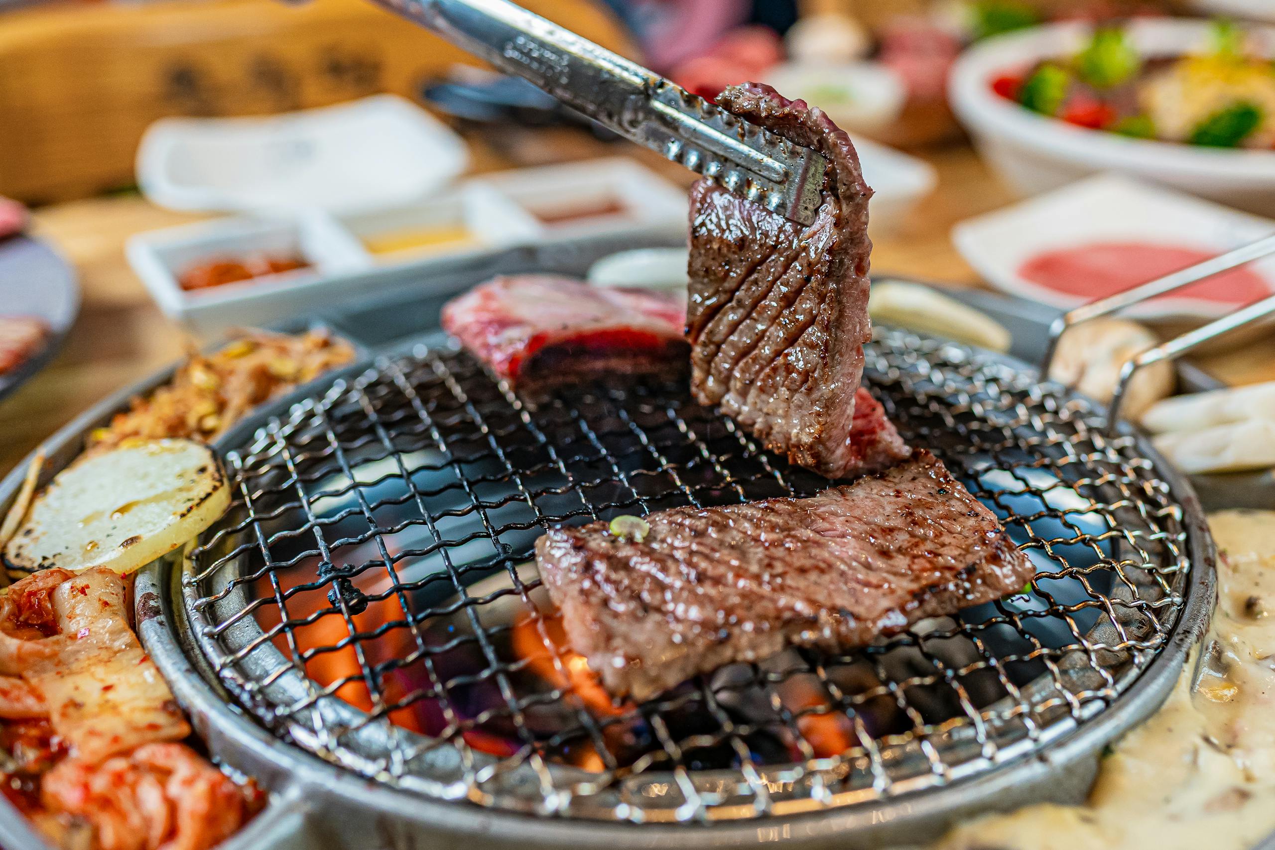 Juicy cuts of meat being grilled on a barbecue with tongs for a delicious meal.
