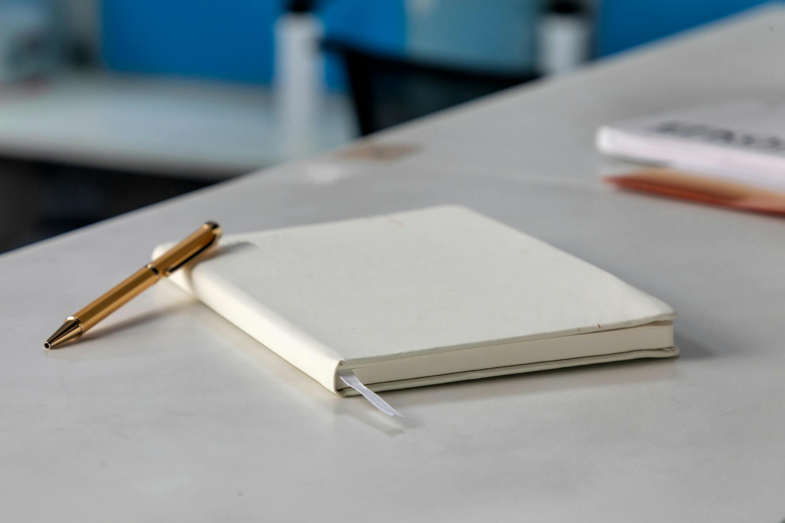 Minimalist white notebook and golden pen on a modern desk setting.