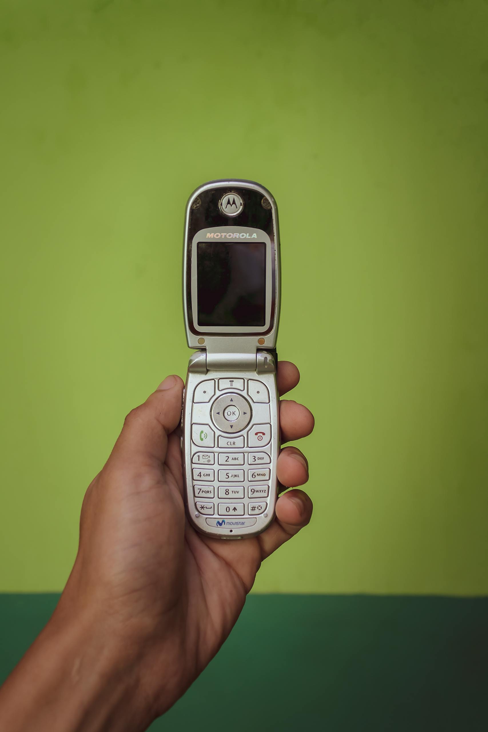 Retro Motorola flip phone held in a hand against a vibrant green background, showcasing nostalgia.