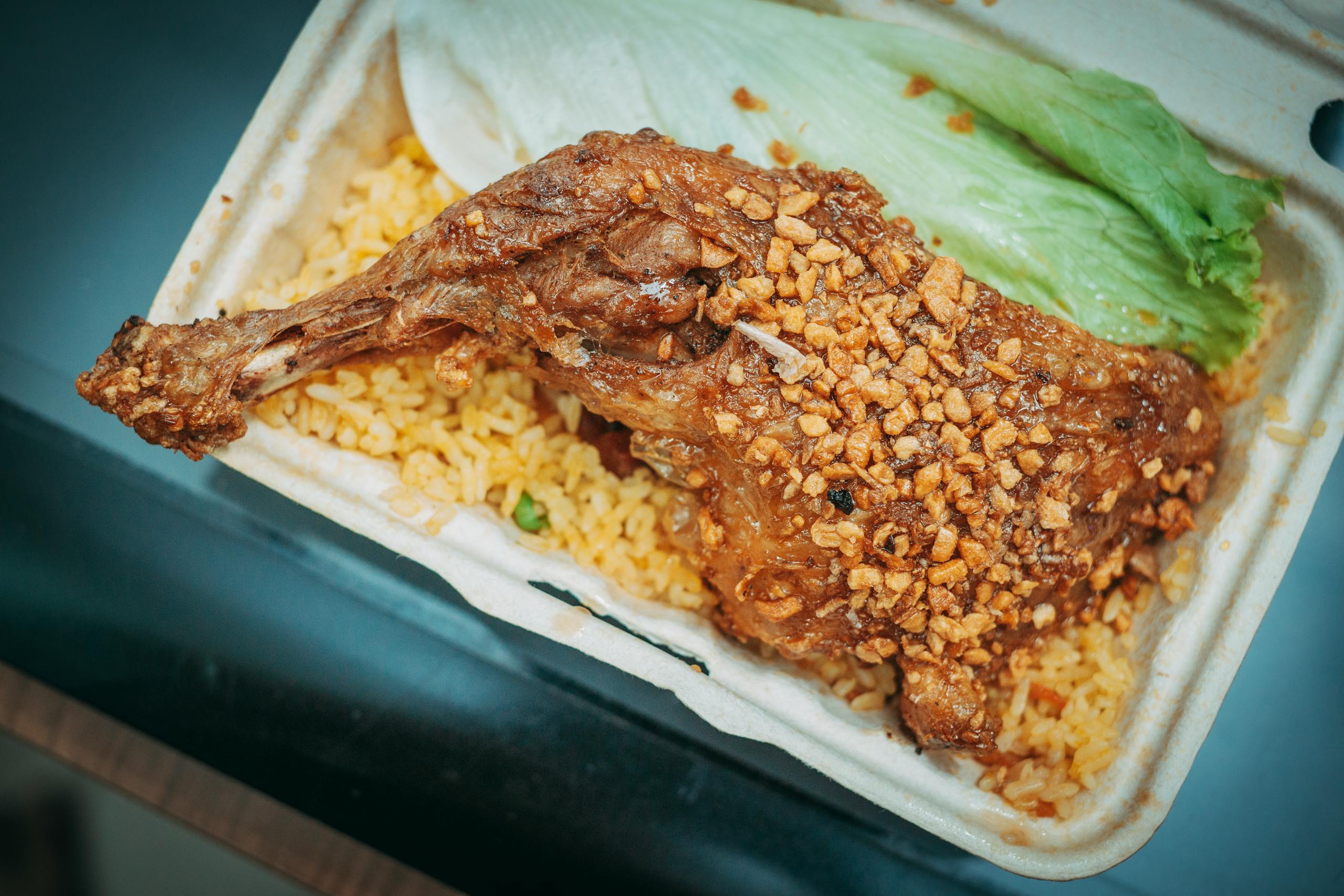 Savor a delicious crispy garlic chicken leg served on a bed of fried rice with fresh lettuce.