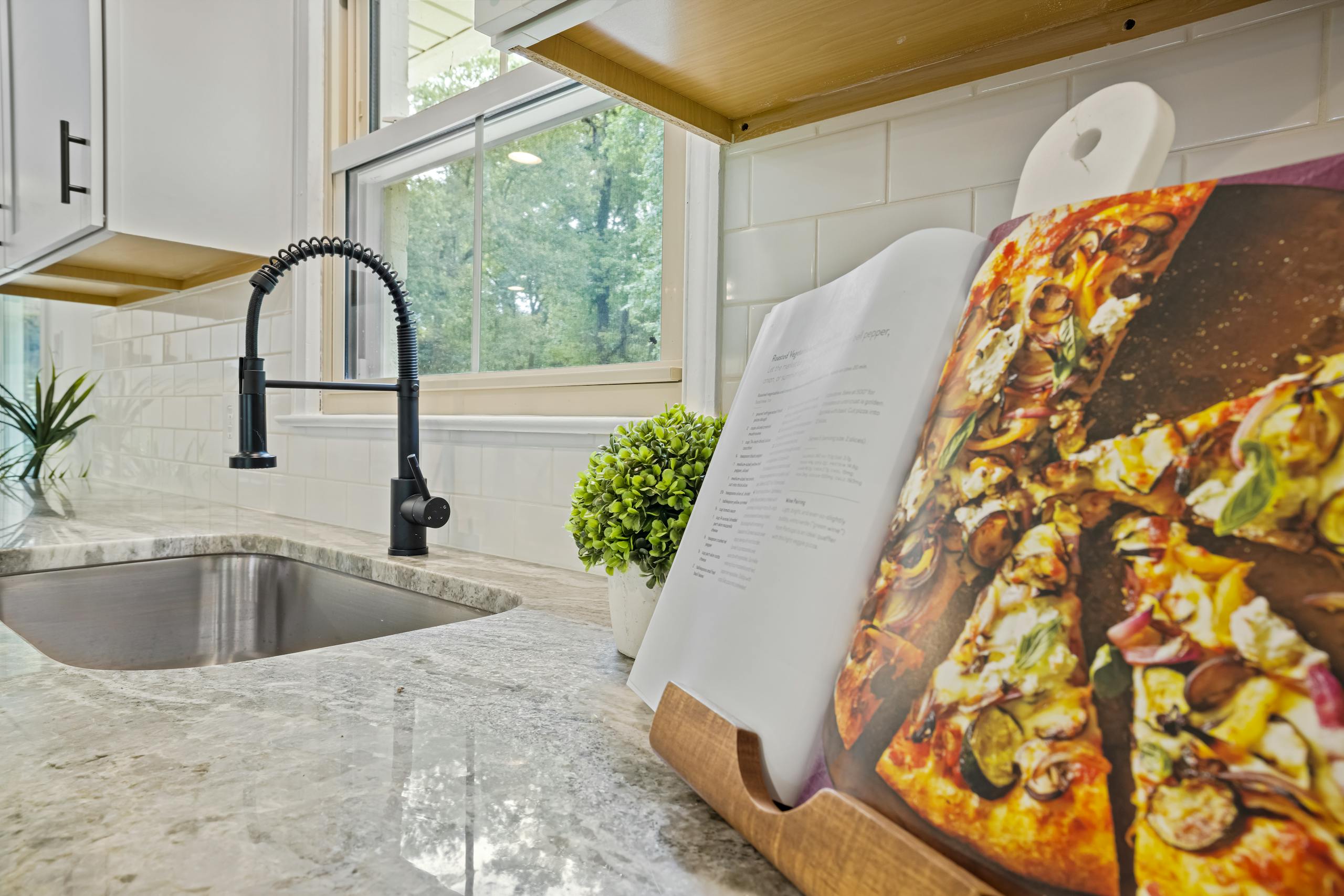 Stylish kitchen featuring a marble countertop, modern sink, and an open cookbook with a pizza recipe.