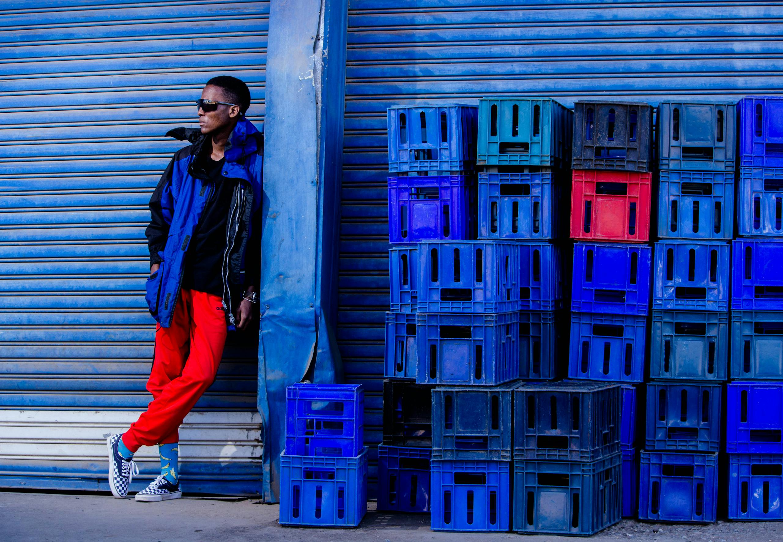 Stylish young man in streetwear standing by blue crates and roll-up door.