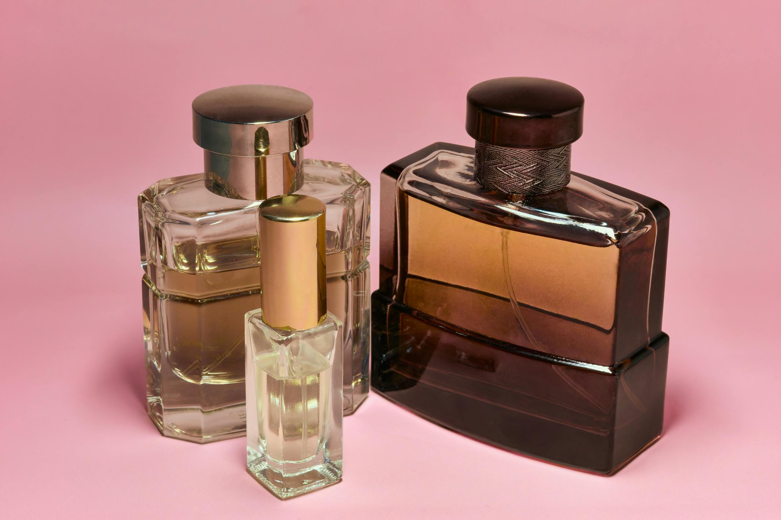 Three stylish perfume bottles with elegant caps on a pink backdrop, capturing a sense of luxury and sophistication.