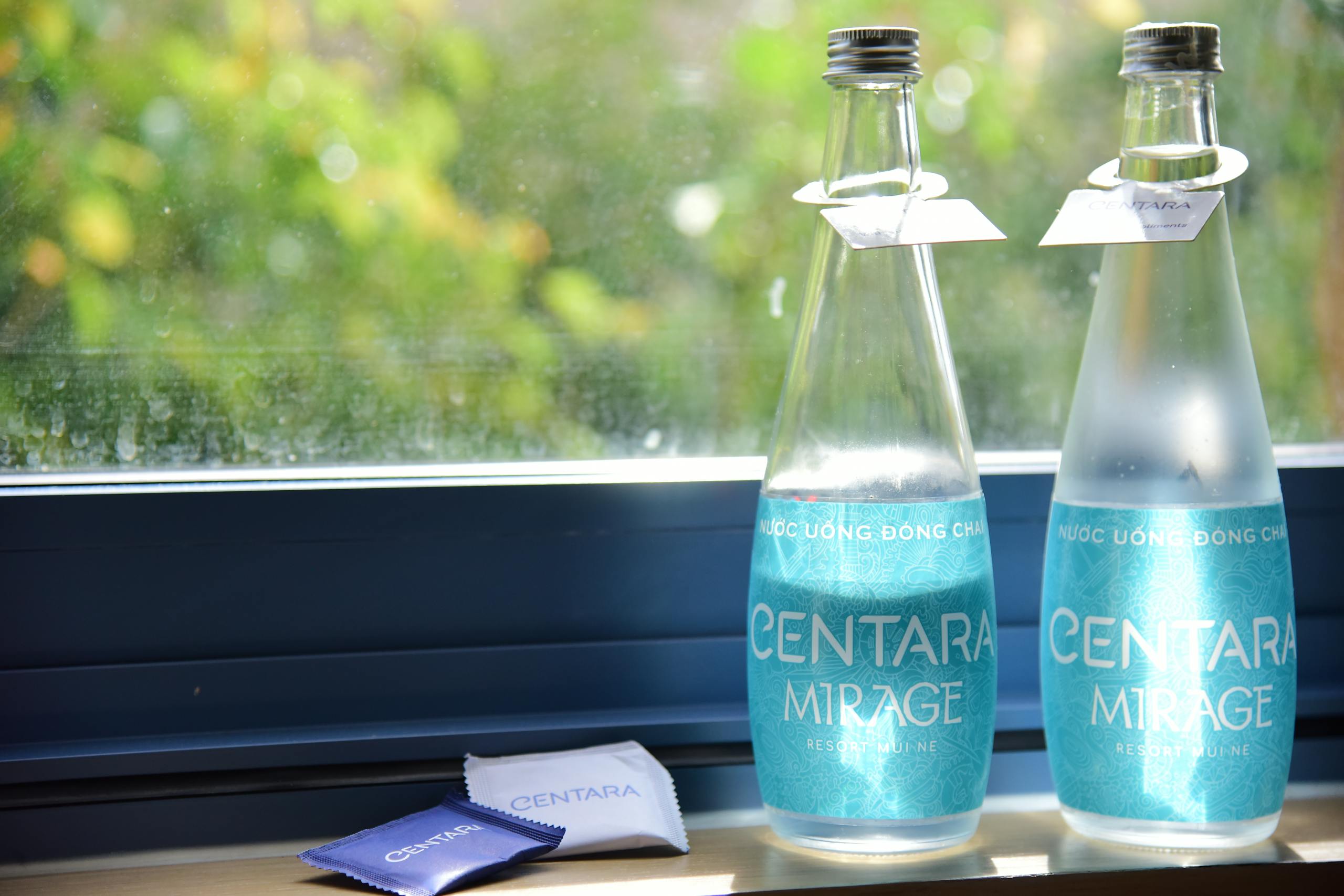 Two Centara Mirage water bottles by a sunlit window with vibrant greenery outside.
