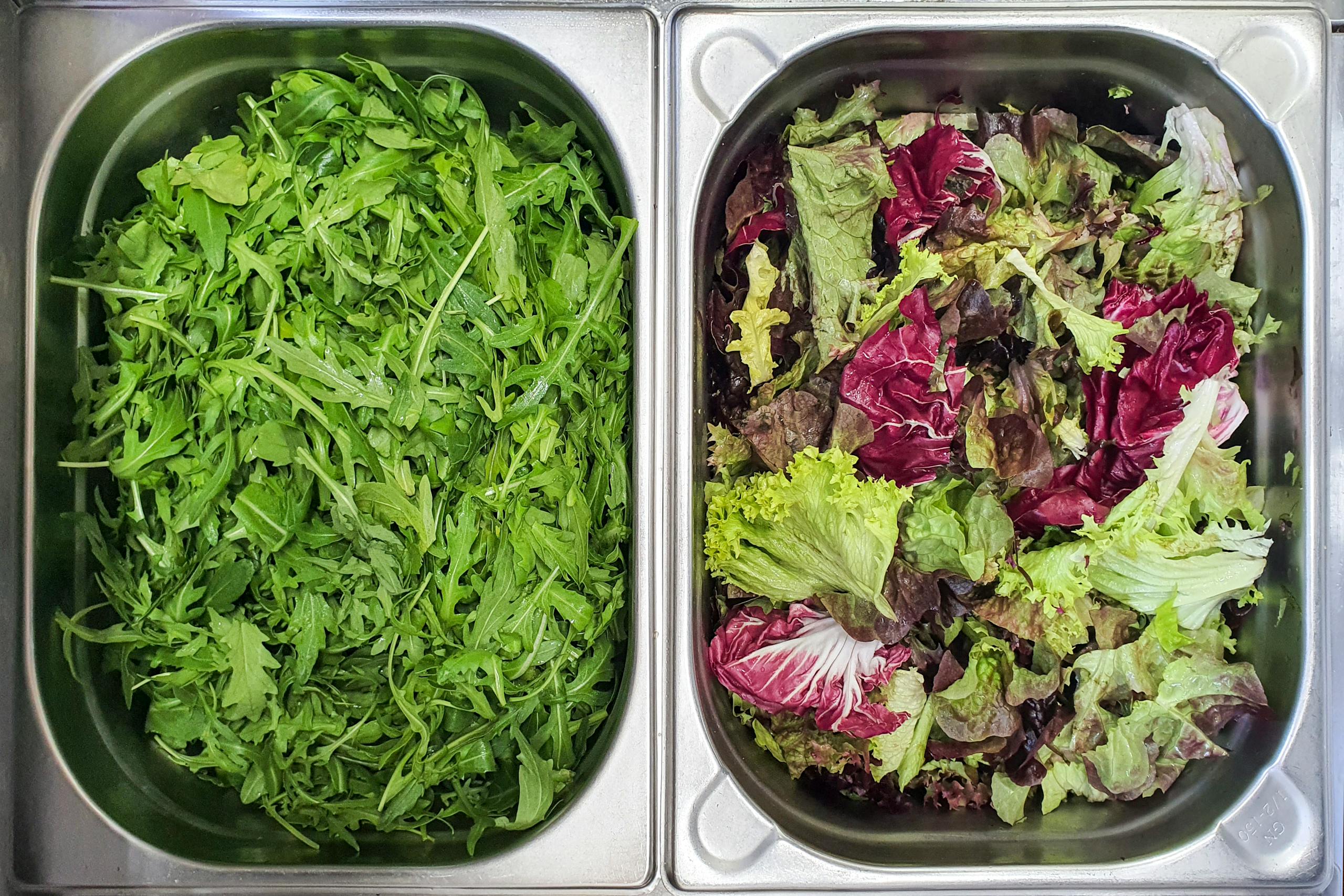 Two trays filled with fresh arugula and mixed lettuce, top view.