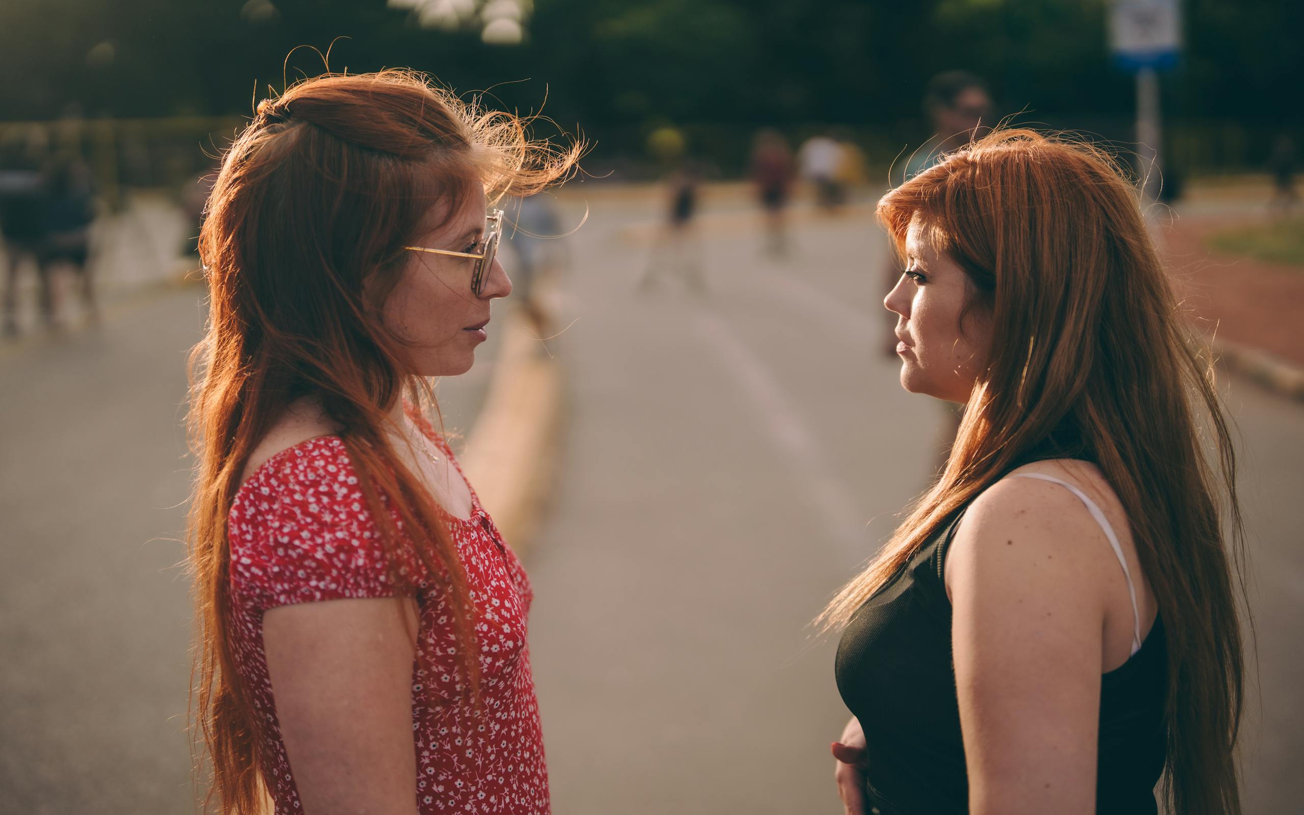 Two women facing each other on a sunny day, engaging in conversation outdoors.