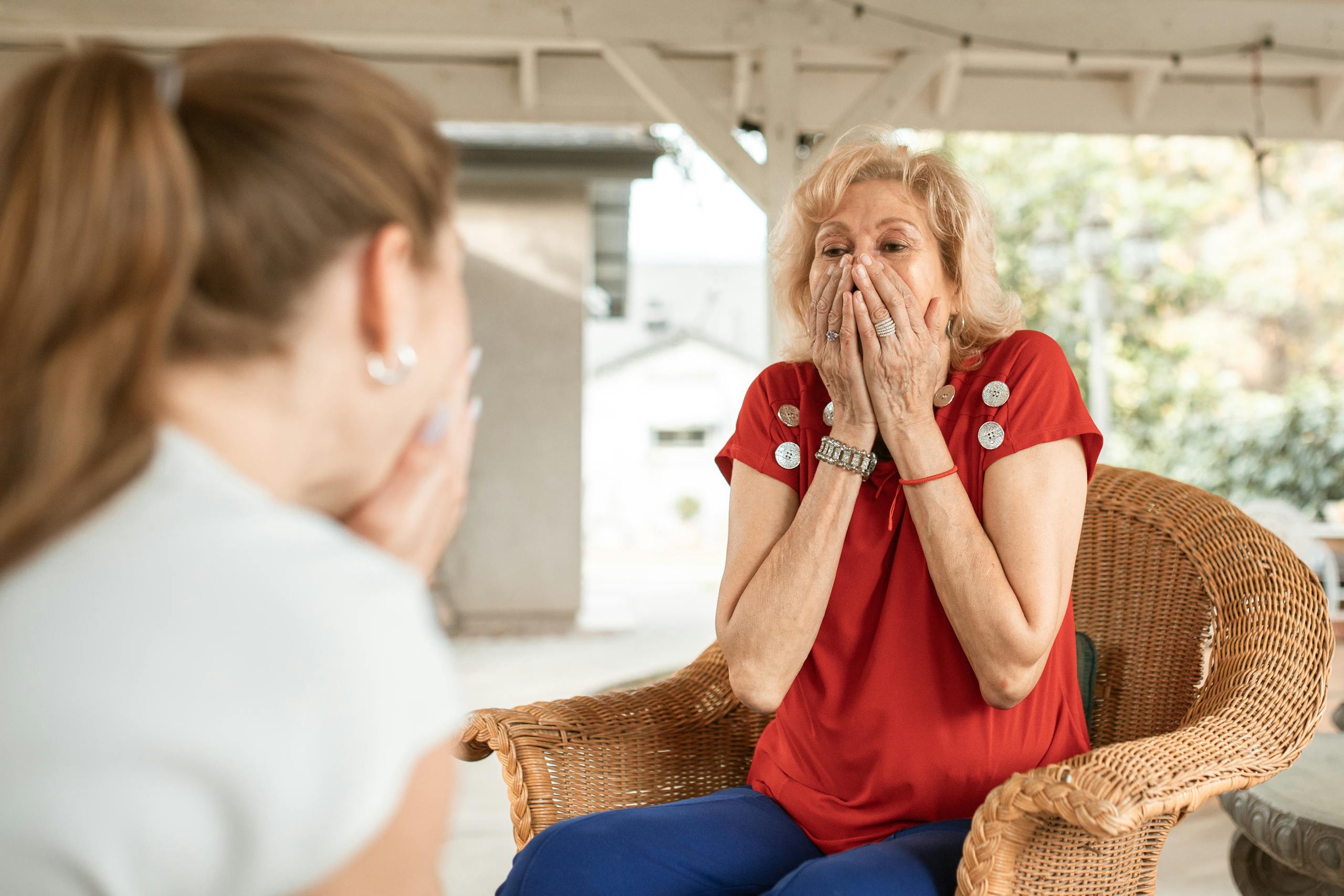 An elderly woman expresses surprise and joy during an outdoor conversation.