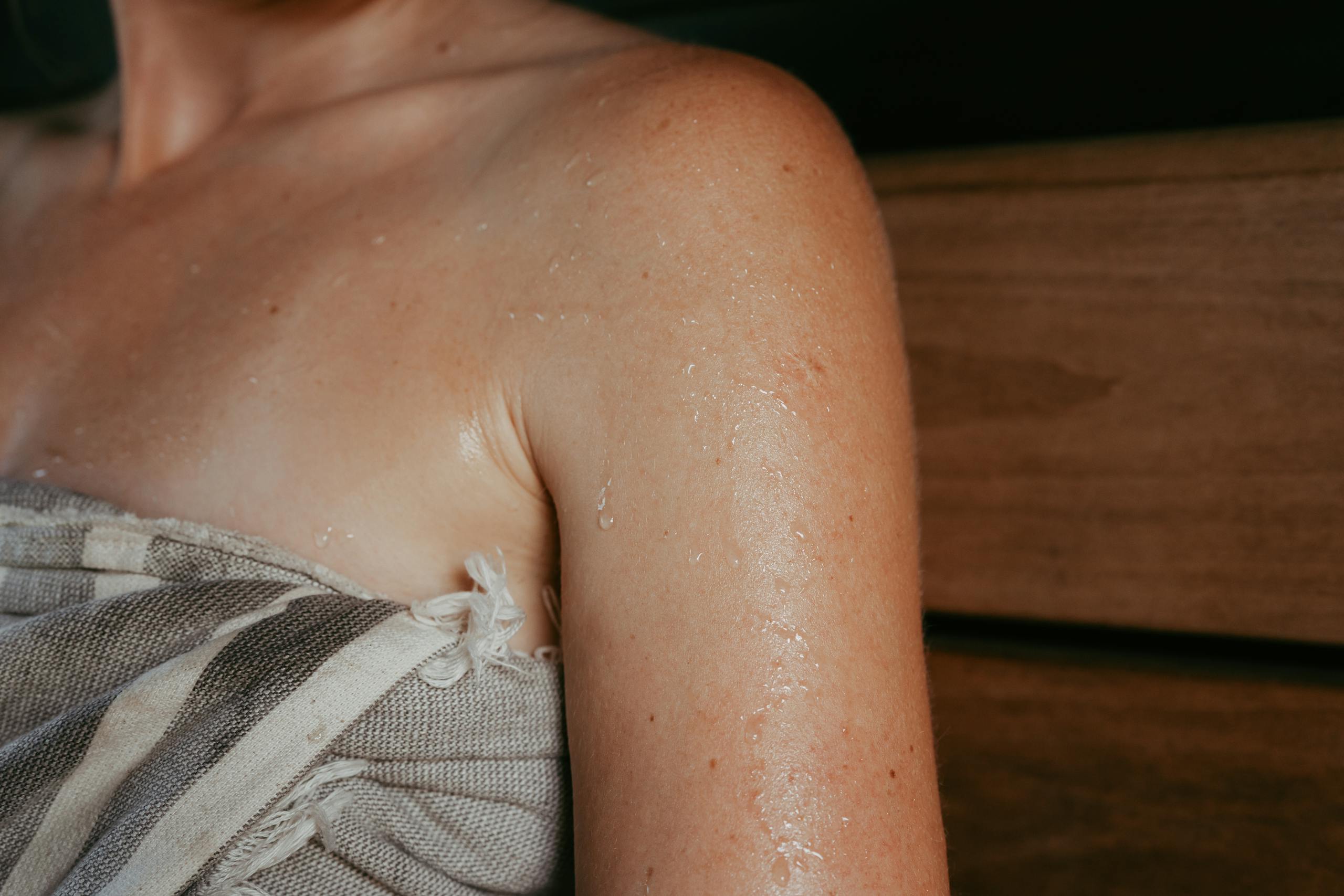 Close-up of a woman with sweat on her skin inside a sauna, highlighting relaxation and wellness.