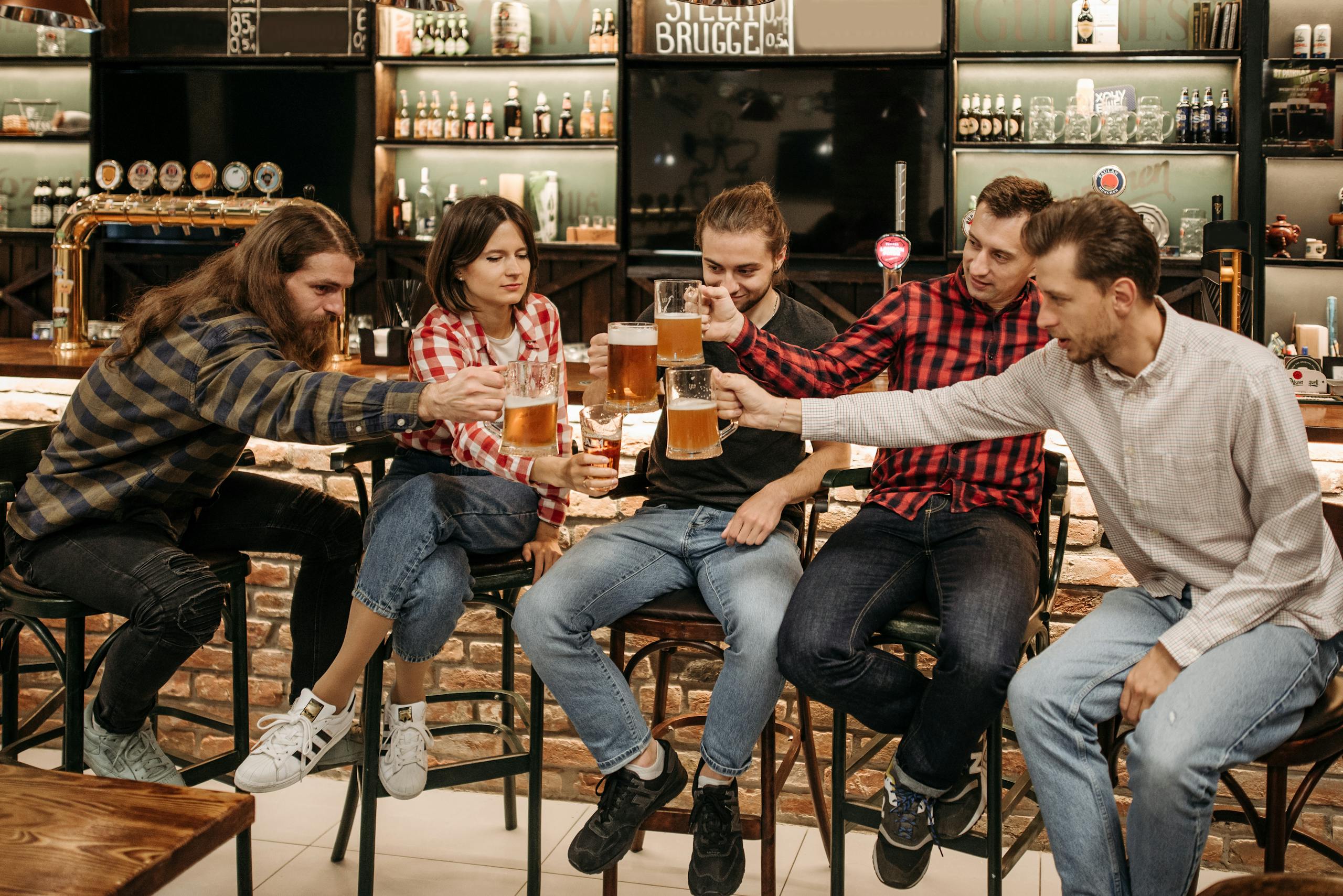 Five friends enjoying a toast with beer mugs at a cozy pub setting indoors.