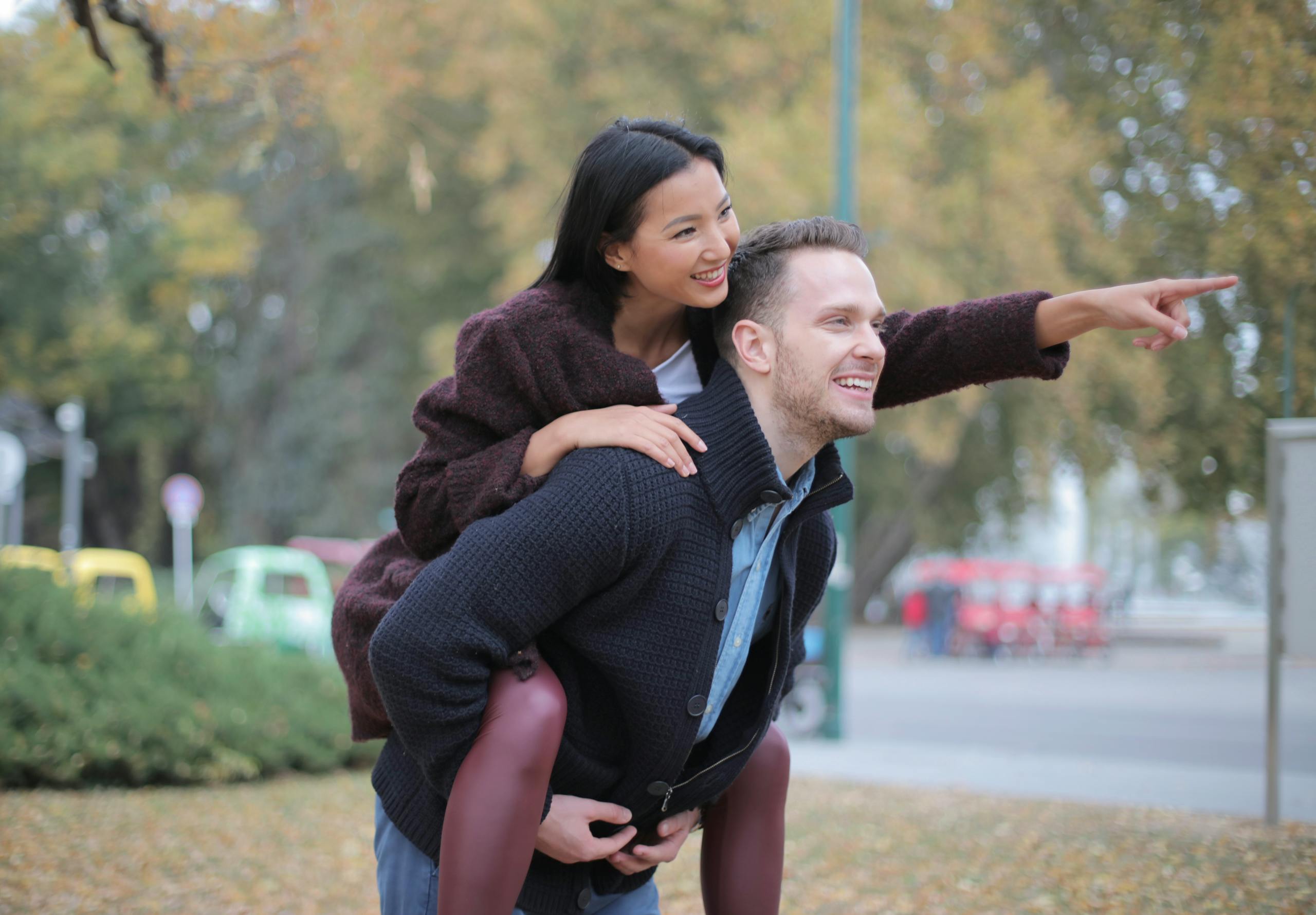 Happy couple enjoying a piggyback ride and pointing in an autumn park outdoors.