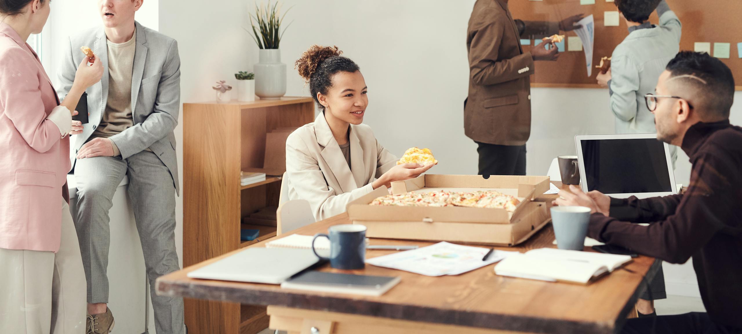 A diverse team enjoys pizza during a casual office lunch break, fostering collaboration.