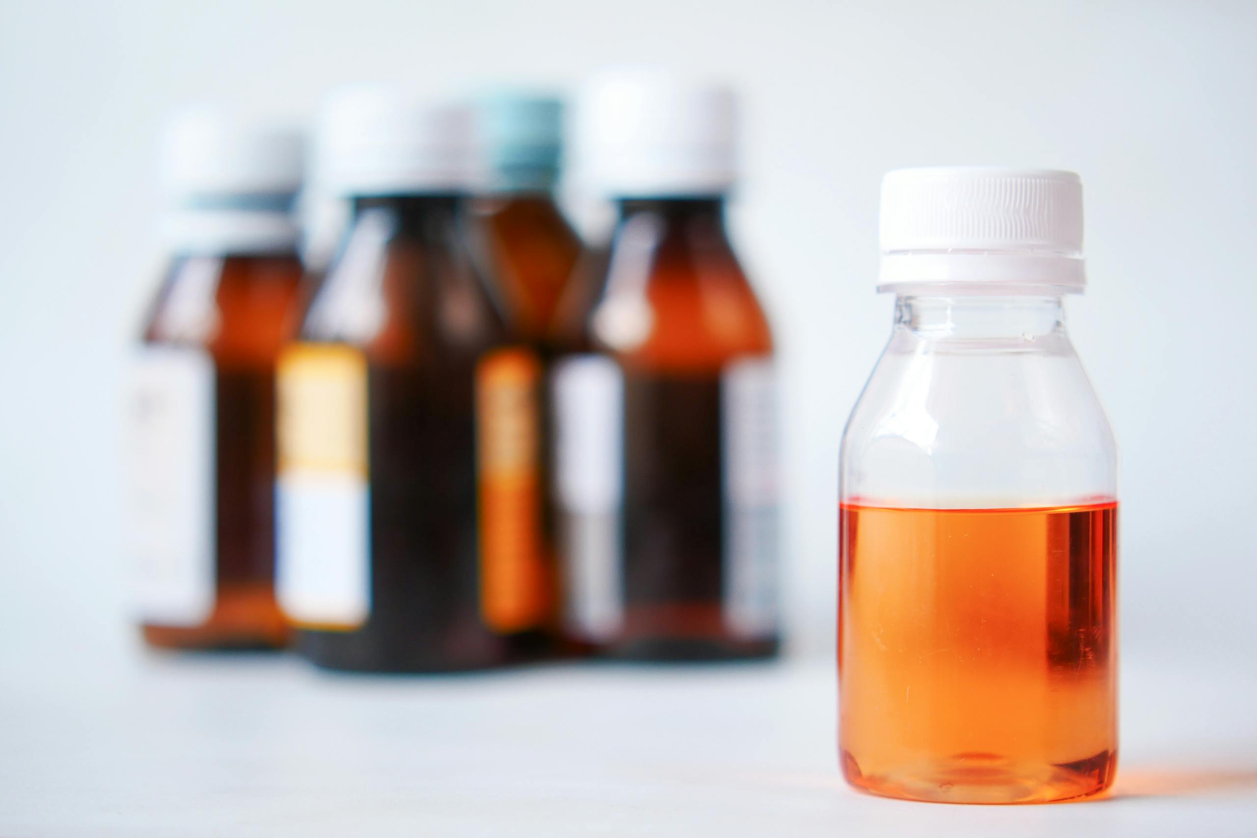 A group of medicine bottles with focus on one filled with orange liquid, ideal for healthcare themes.