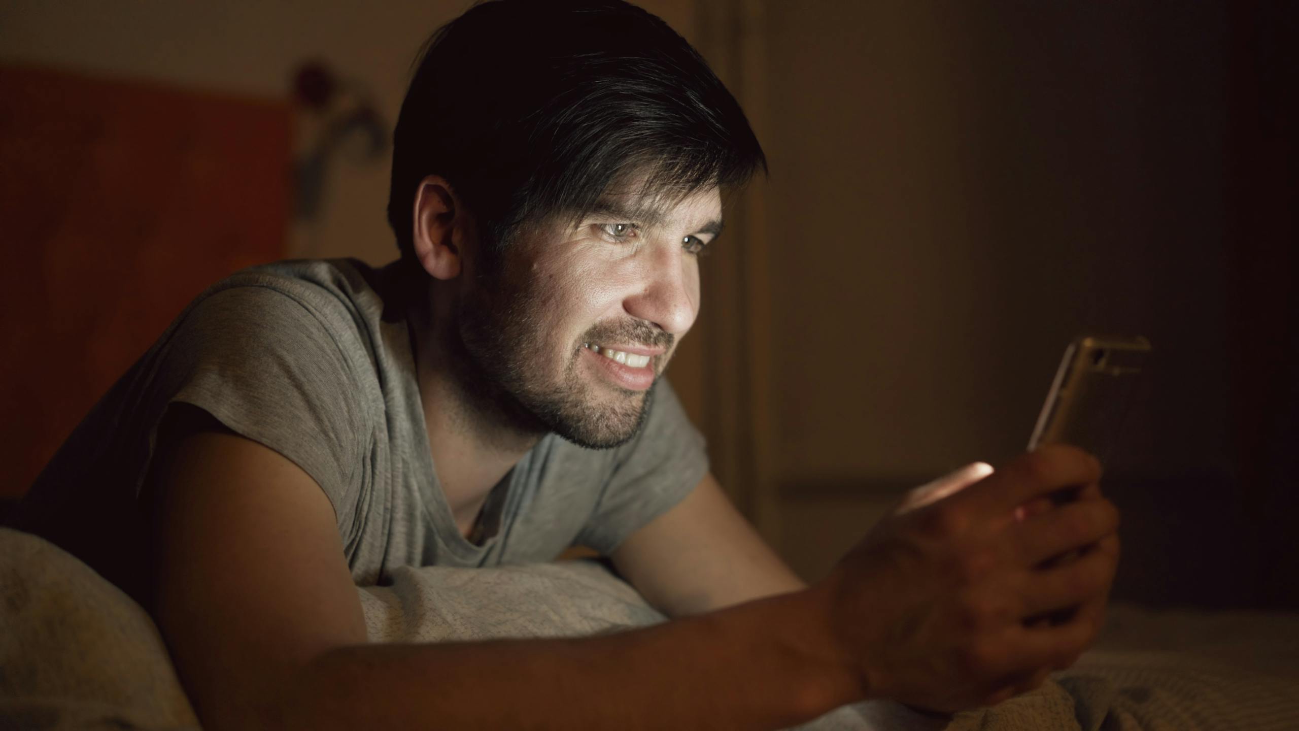 A man enjoys a late-night phone screen, illuminating his face.