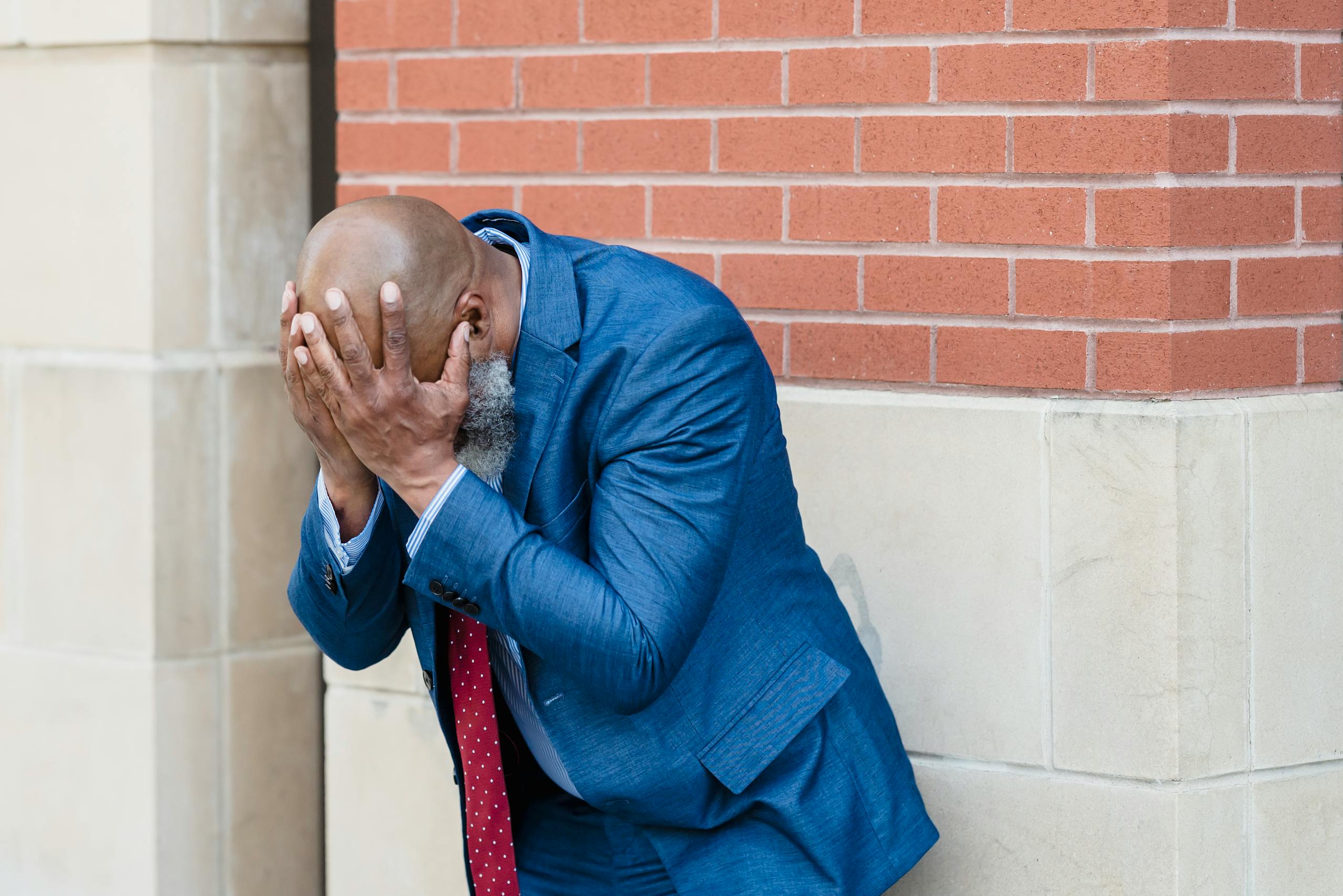 Businessman in blue suit shows stress and concern against urban background.