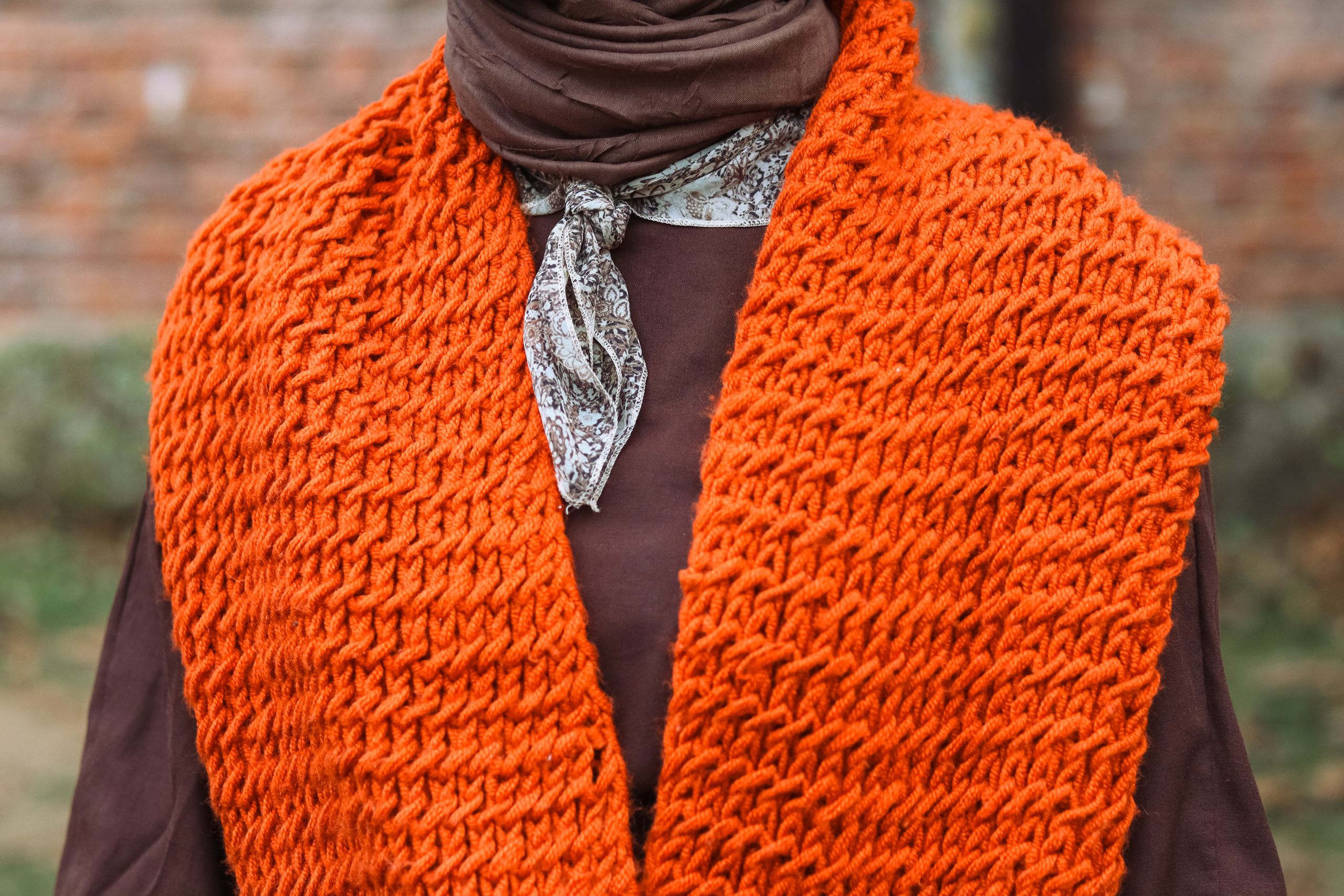 Close-up of a stylish orange knit scarf and brown outfit, perfect for fall fashion enthusiasts.