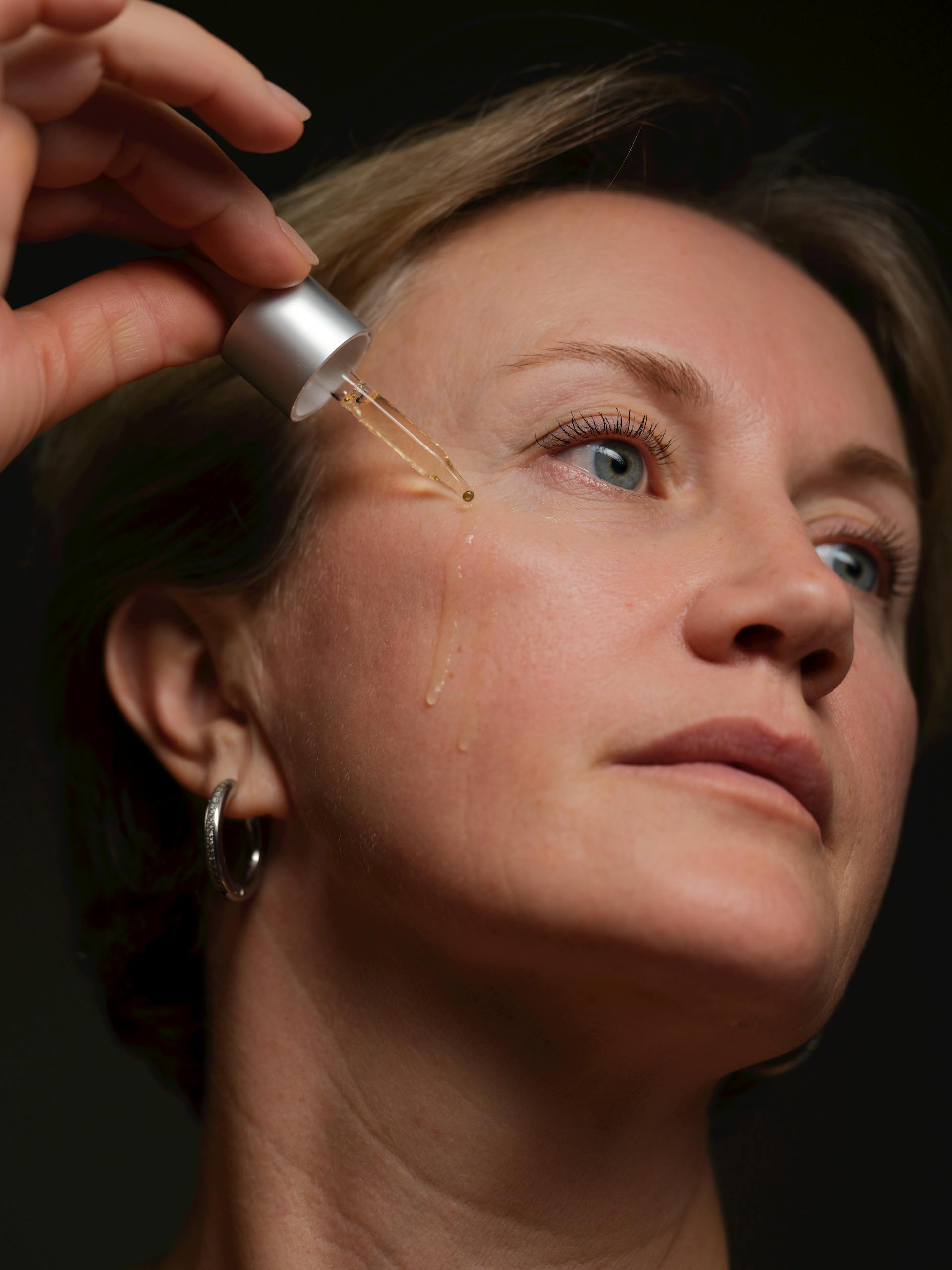 Close-up of woman applying facial serum with a dropper, focusing on skincare and beauty.