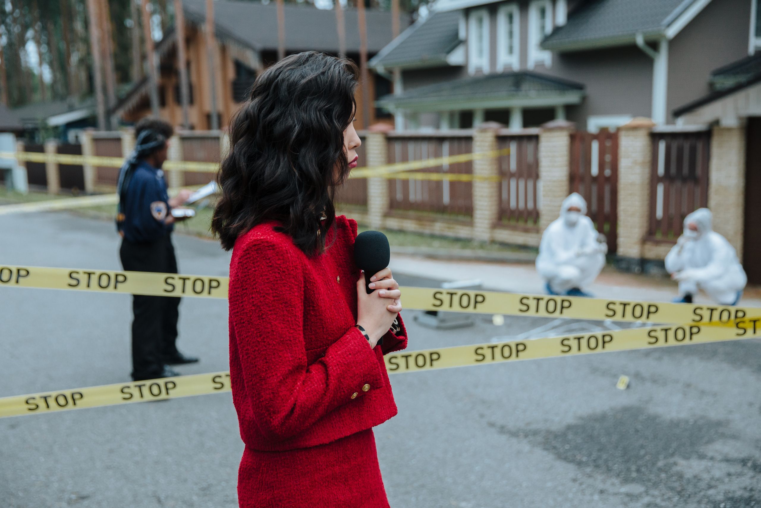 A female journalist is reporting live on a crime scene investigation with police presence outdoors.