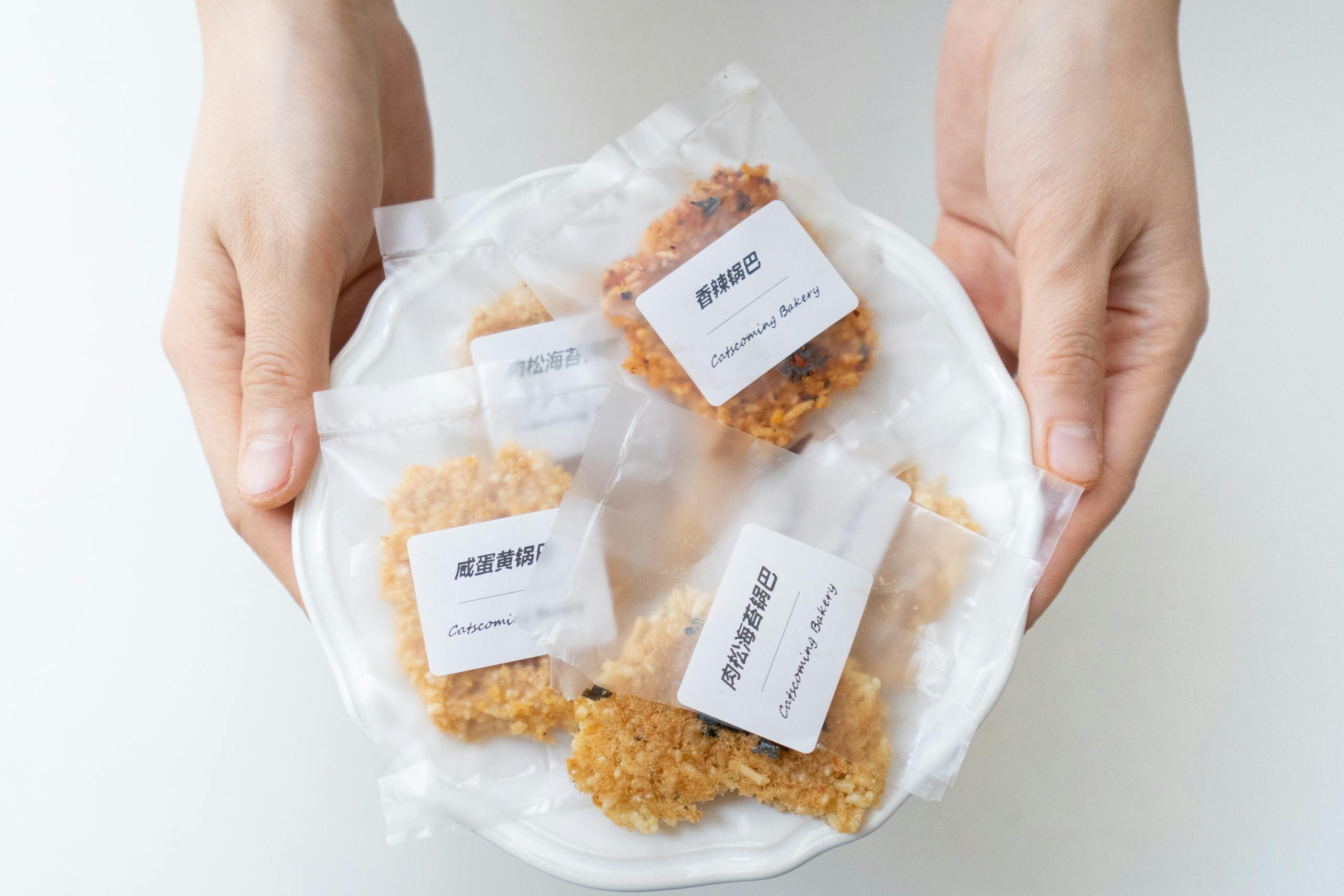 From above of crop anonymous person showing ceramic plate with delicious cookies in transparent packages with label on white surface