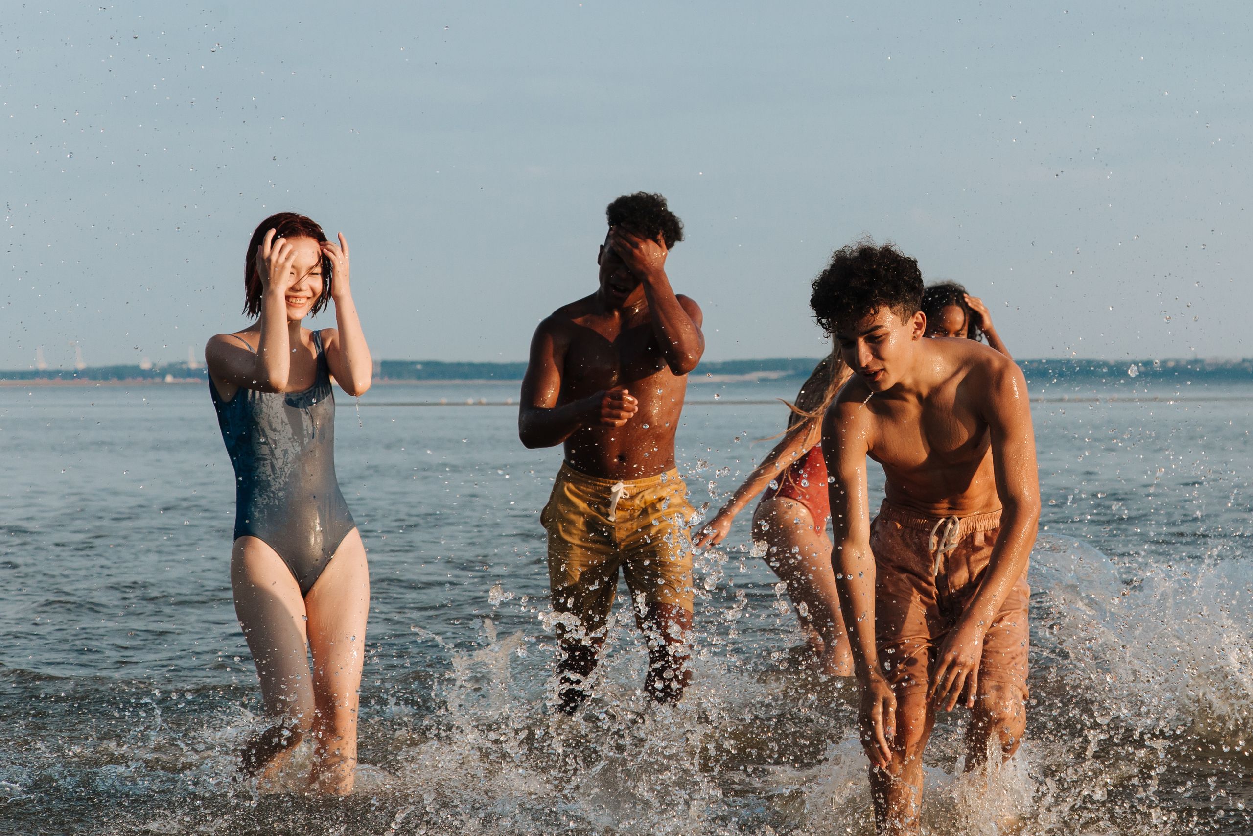 Group of teenagers playing and splashing in the sea, embracing a joyful summer day by the beach.
