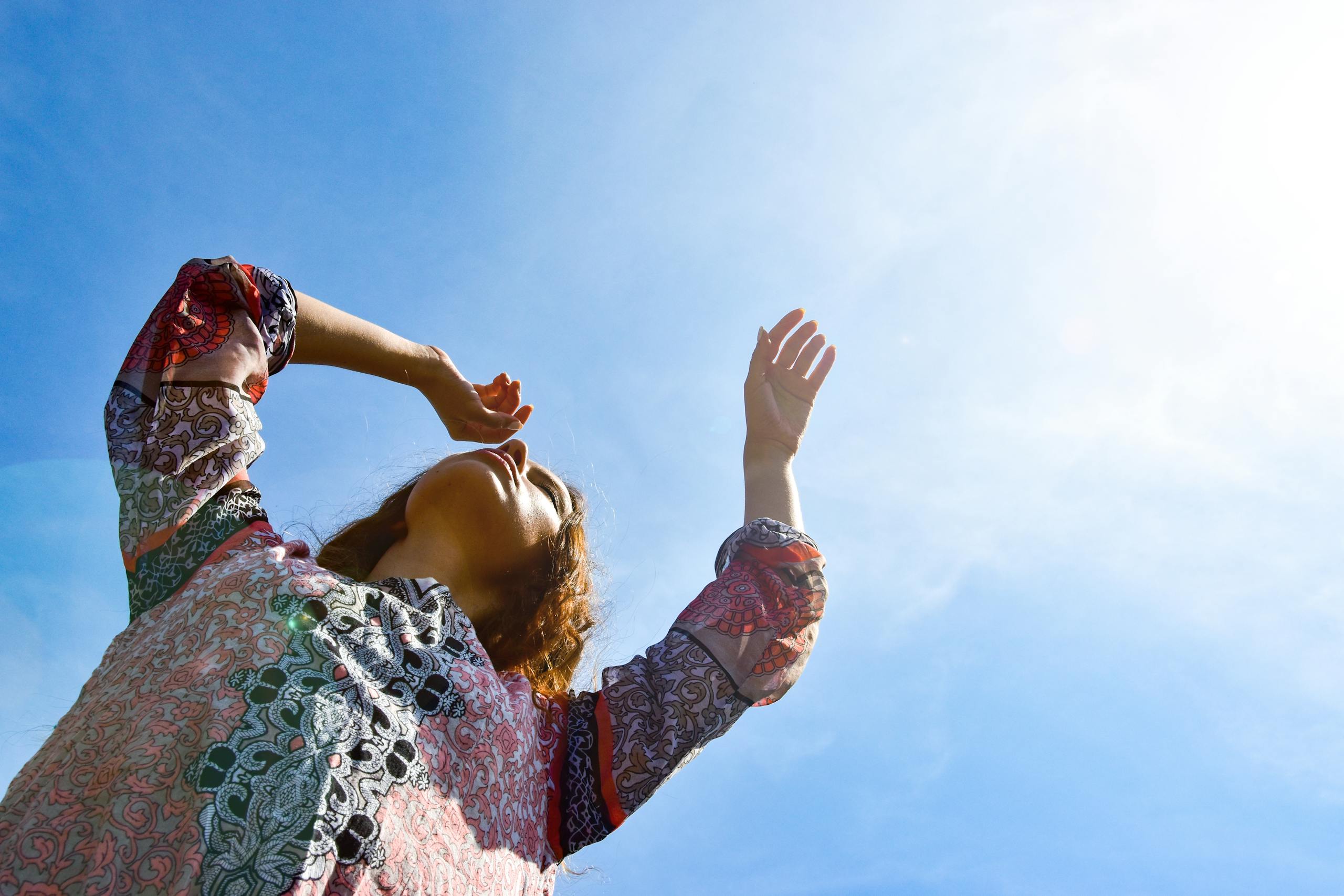 Low angle view of a woman with arms raised against a bright sunny sky.