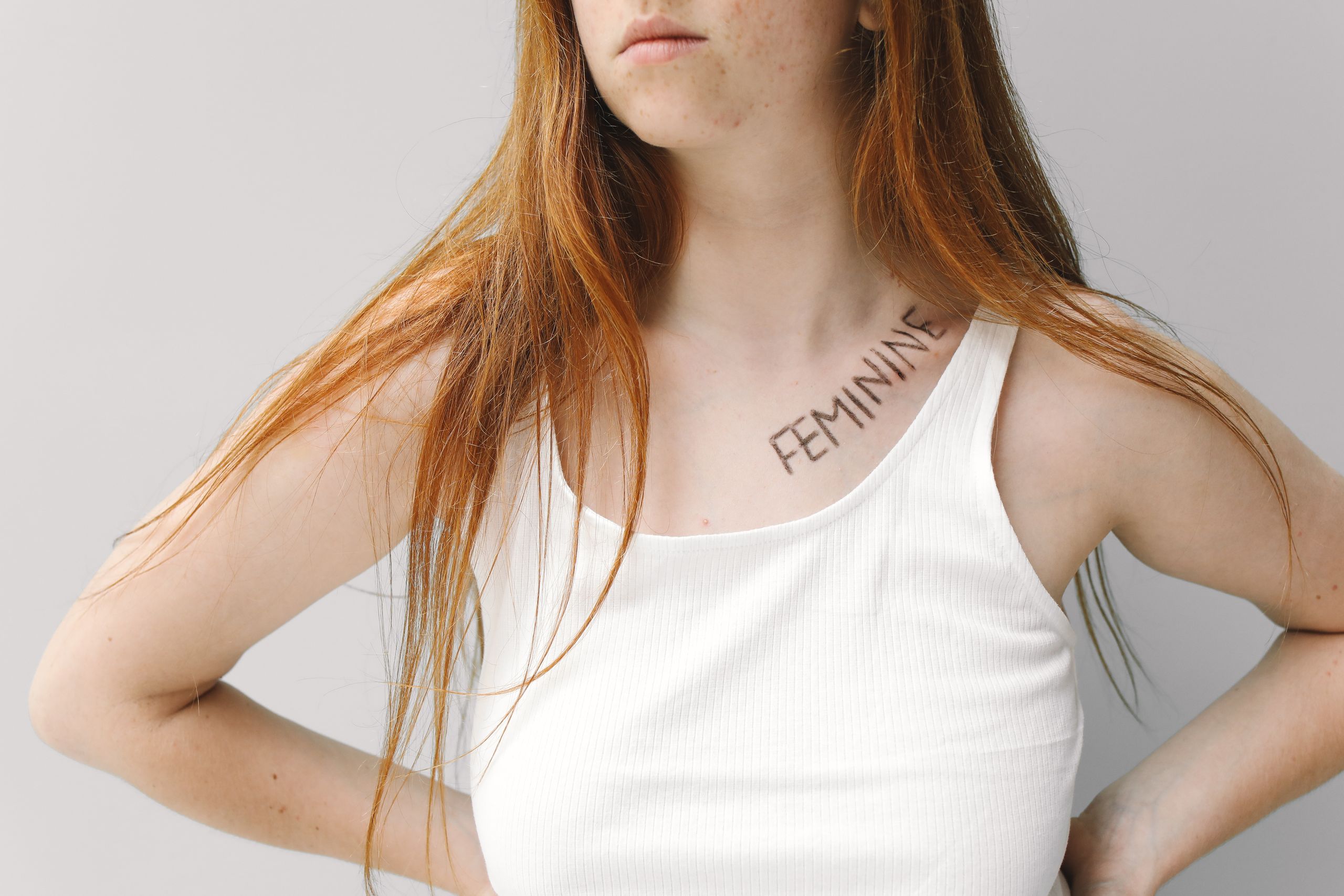 Portrait of a young woman with the word 'feminine' written on her collarbone, expressing individuality and empowerment.