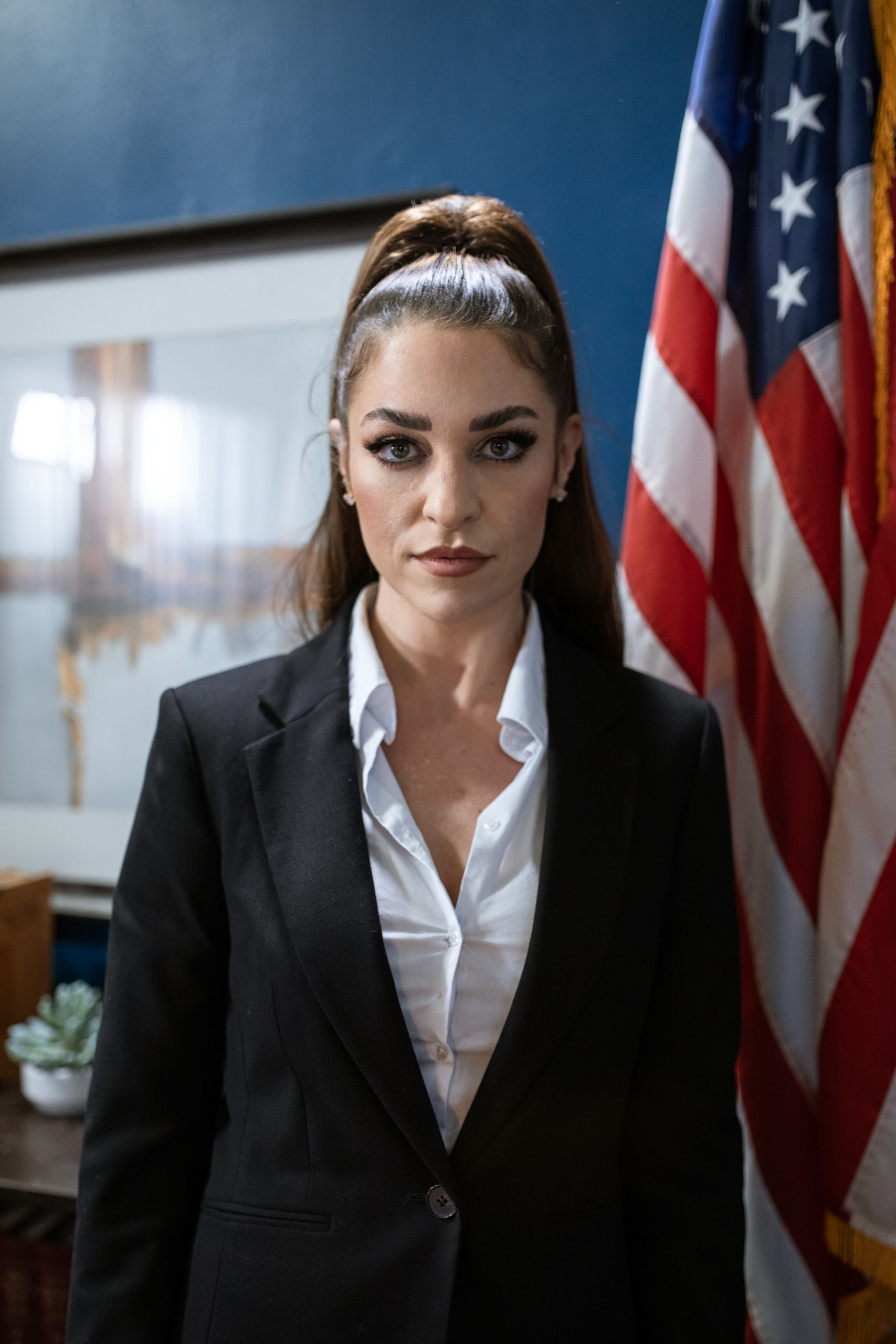 Professional woman in a black blazer standing by the American flag, exuding confidence.